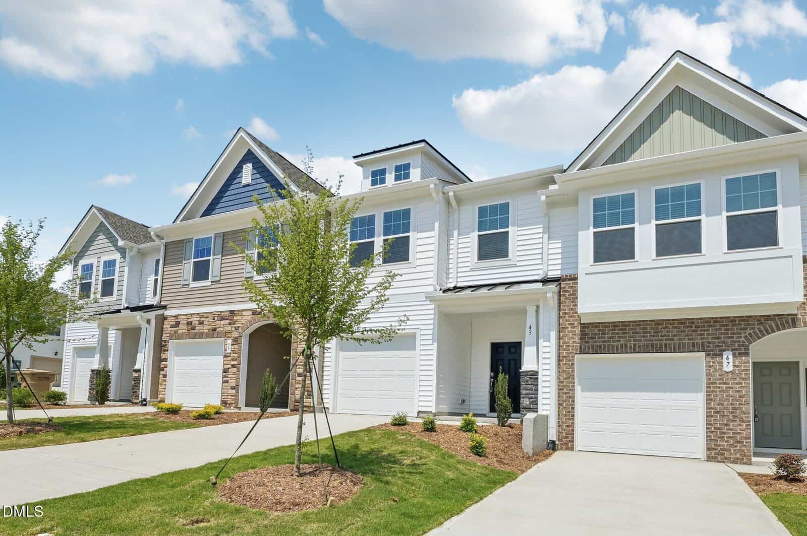 A row of modern suburban townhouses at 201 Carnaby Lane, Franklinton, with white and brick exteriors, double garages, and young trees planted in front, under a partly cloudy blue sky.