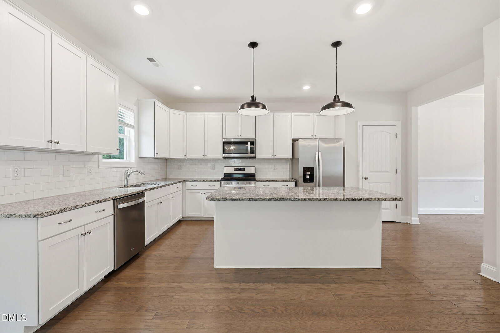 Modern kitchen with white cabinets, granite countertops, stainless steel appliances, a central island, pendant lights, hardwood floor, and a view into an adjacent room.