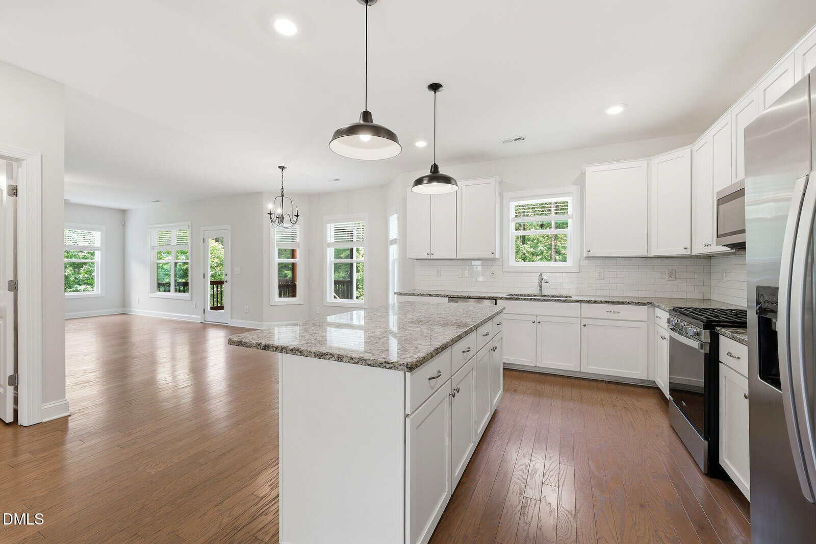 Modern kitchen with white cabinets, granite island, stainless steel appliances, and pendant lighting, open to a spacious living area with hardwood floors and large windows letting in natural light.