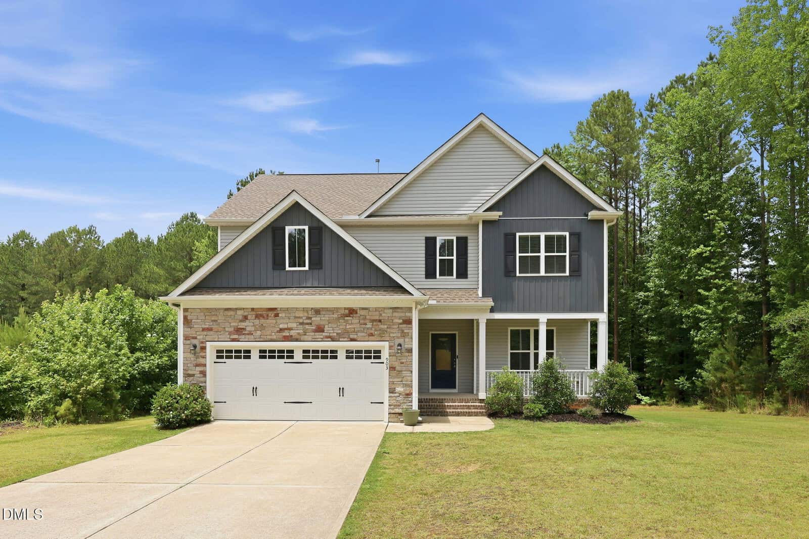 Charming two-story suburban house at 903 Weatherby Lane, Creedmoor, featuring gray siding, stone accents, a front porch, double garage, manicured lawn, and mature trees under a blue sky.