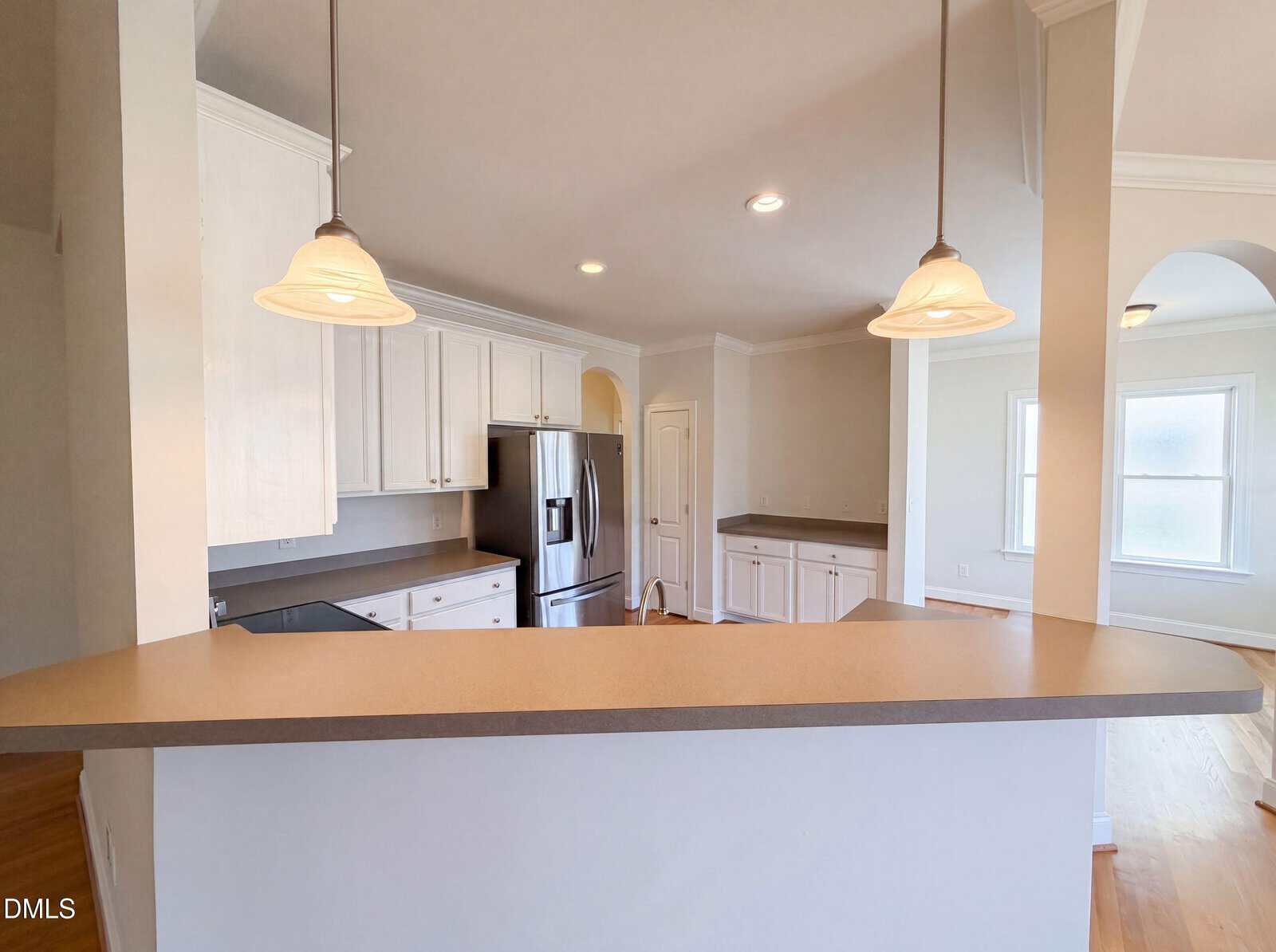 Modern kitchen with white cabinets, stainless steel appliances, gray countertops, and two pendant lights over a breakfast bar. There is a doorway and a window visible in the background.