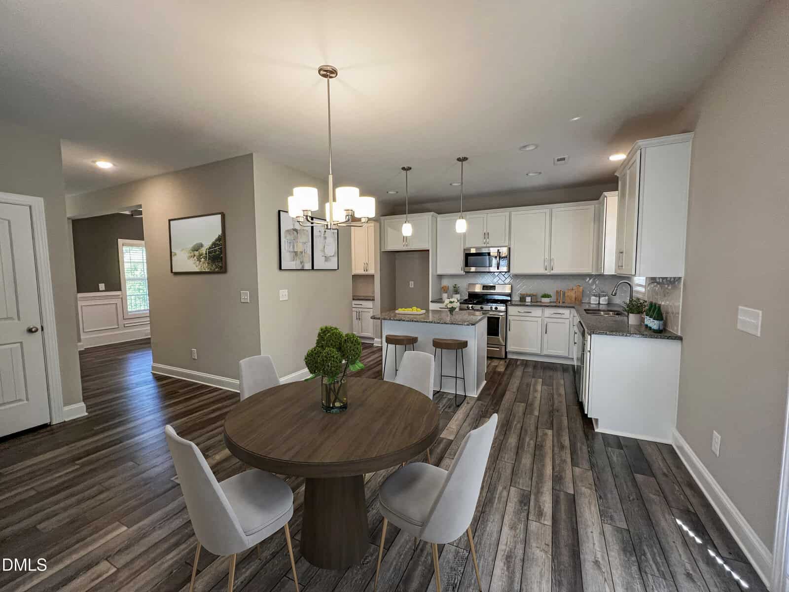Modern kitchen and dining area with wood floors, white cabinets, round table with four chairs, pendant lighting, and stainless steel appliances, all in a bright, open layout.