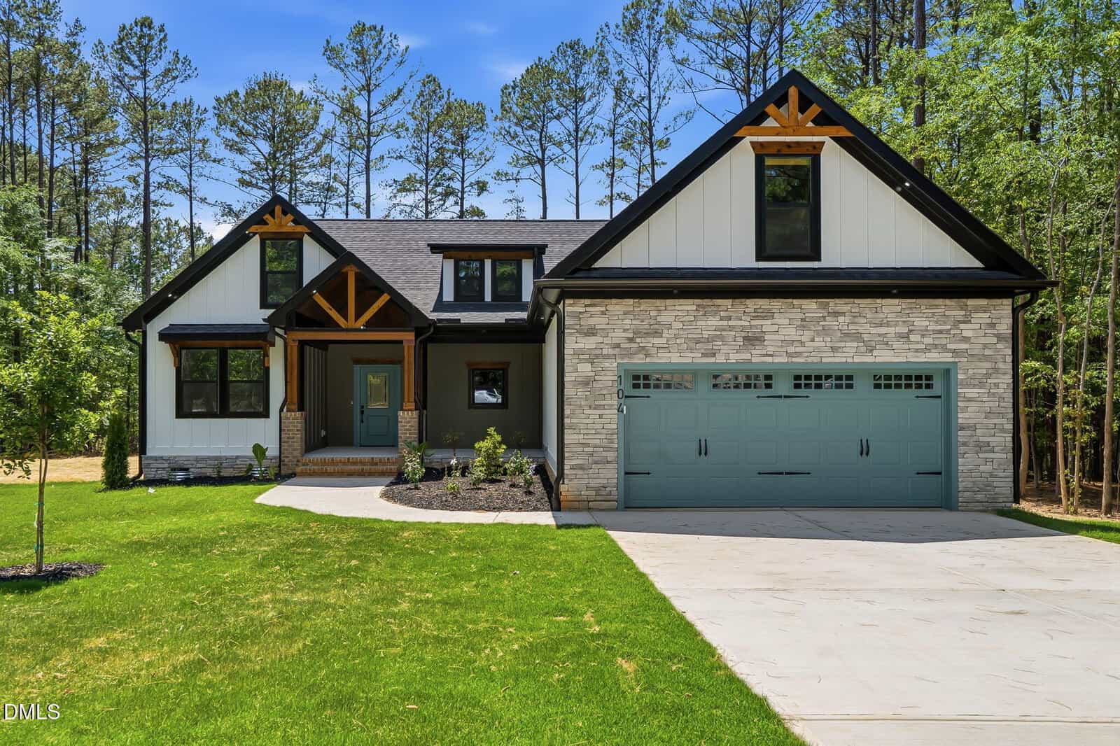 A modern house at 104 Medicine Cove, Louisburg, with white siding, stone accents, dark wood trim, and a teal double garage door, is surrounded by green grass, landscaping, and tall pine trees in the background.