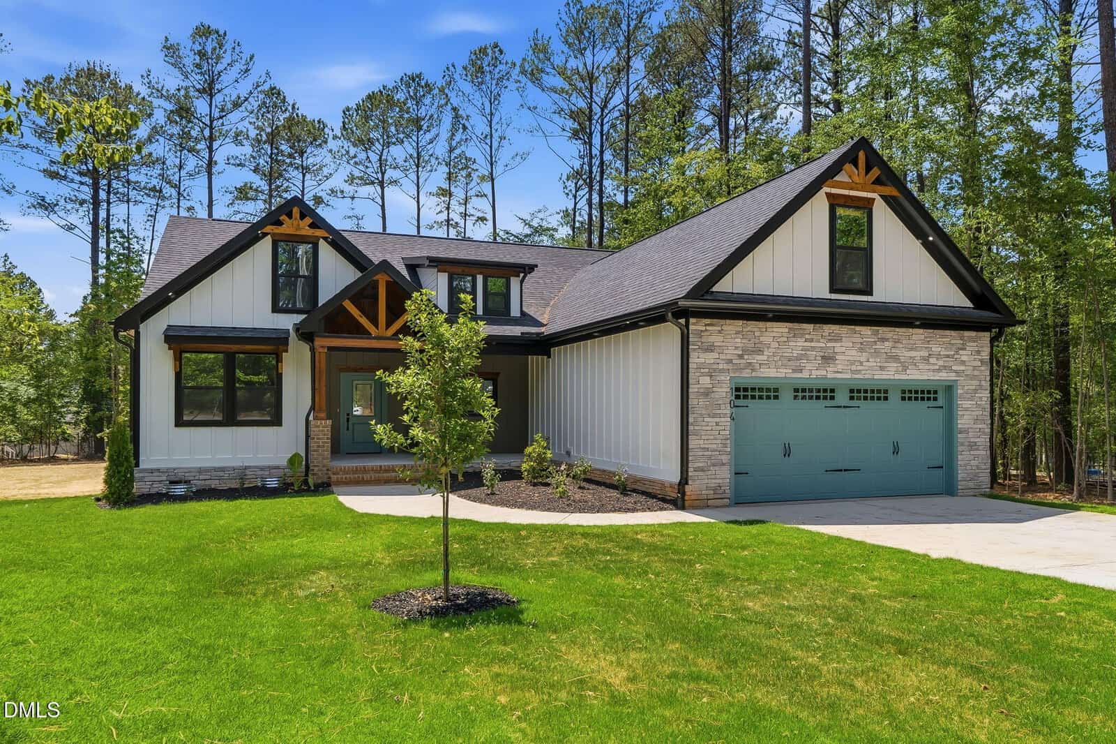 Modern two-story house with a light brick and white board-and-batten exterior, teal garage door, wood accents, and a covered front porch, surrounded by a green lawn and tall trees in the background.