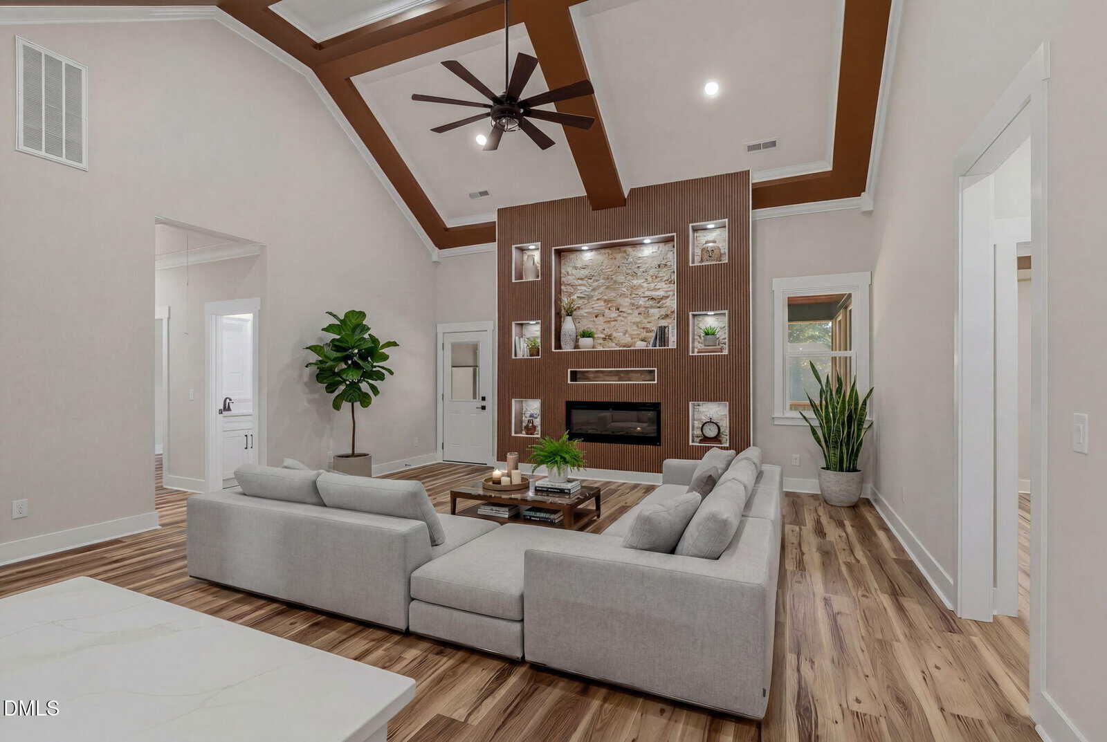 Modern living room with a gray sectional sofa, wood flooring, large potted plants, and a wall-mounted TV above a fireplace set in a wood-paneled feature wall with built-in shelves and recessed lighting.