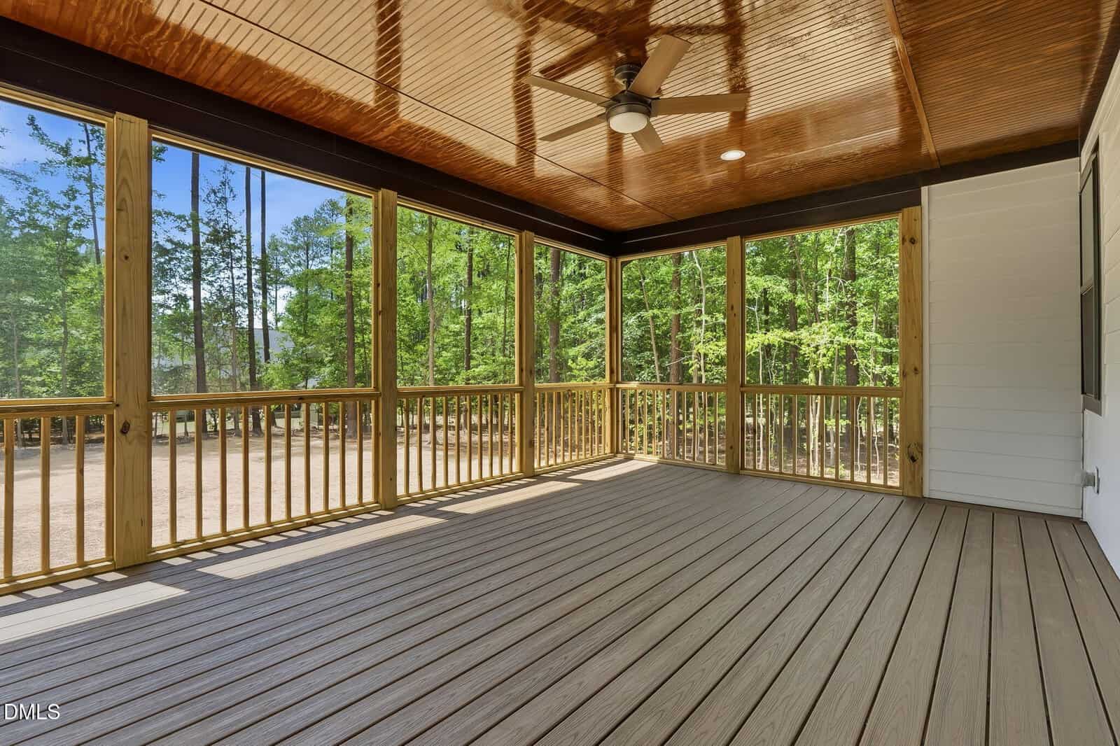 Spacious screened-in porch with wood floors and ceiling, ceiling fan, and views of trees and a dirt yard outside. Natural light fills the area.