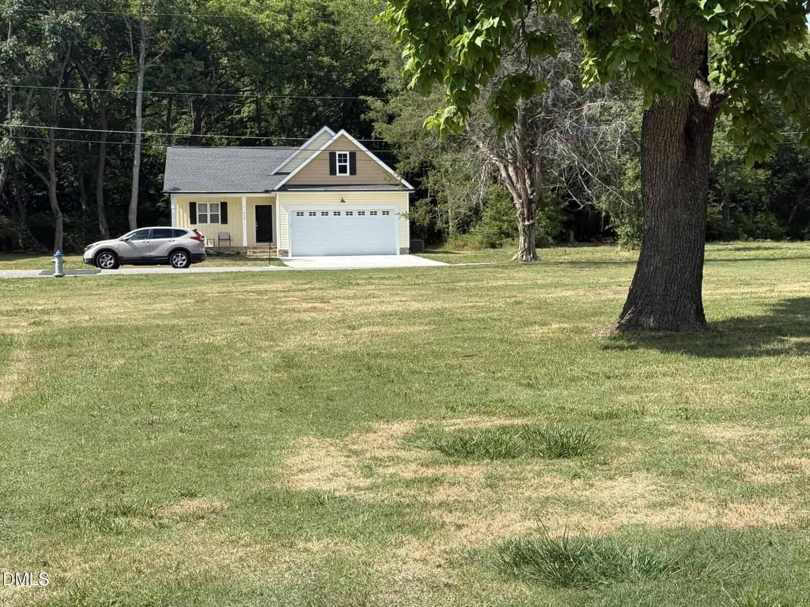A small beige house at 509 Hicksmill Road in Oxford features a two-car garage at the edge of a large grassy yard, bordered by trees. A silver car is parked in the driveway, and a leafy tree stands in the foreground.