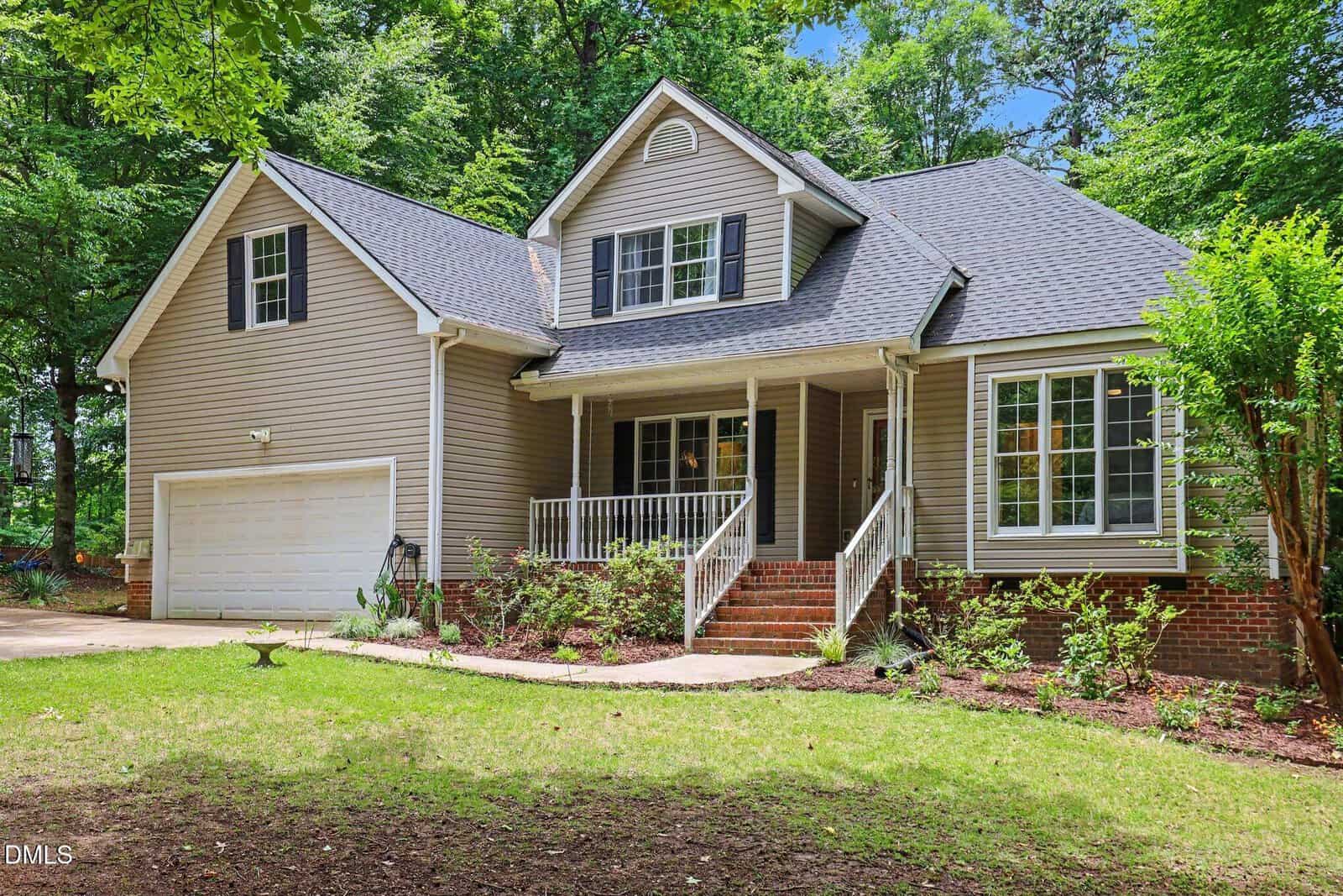 A two-story house at 113 Richland Drive in Youngsville features beige siding, a covered front porch with white railings, dark gray roof, attached two-car garage, brick steps, and a landscaped front yard surrounded by green trees.