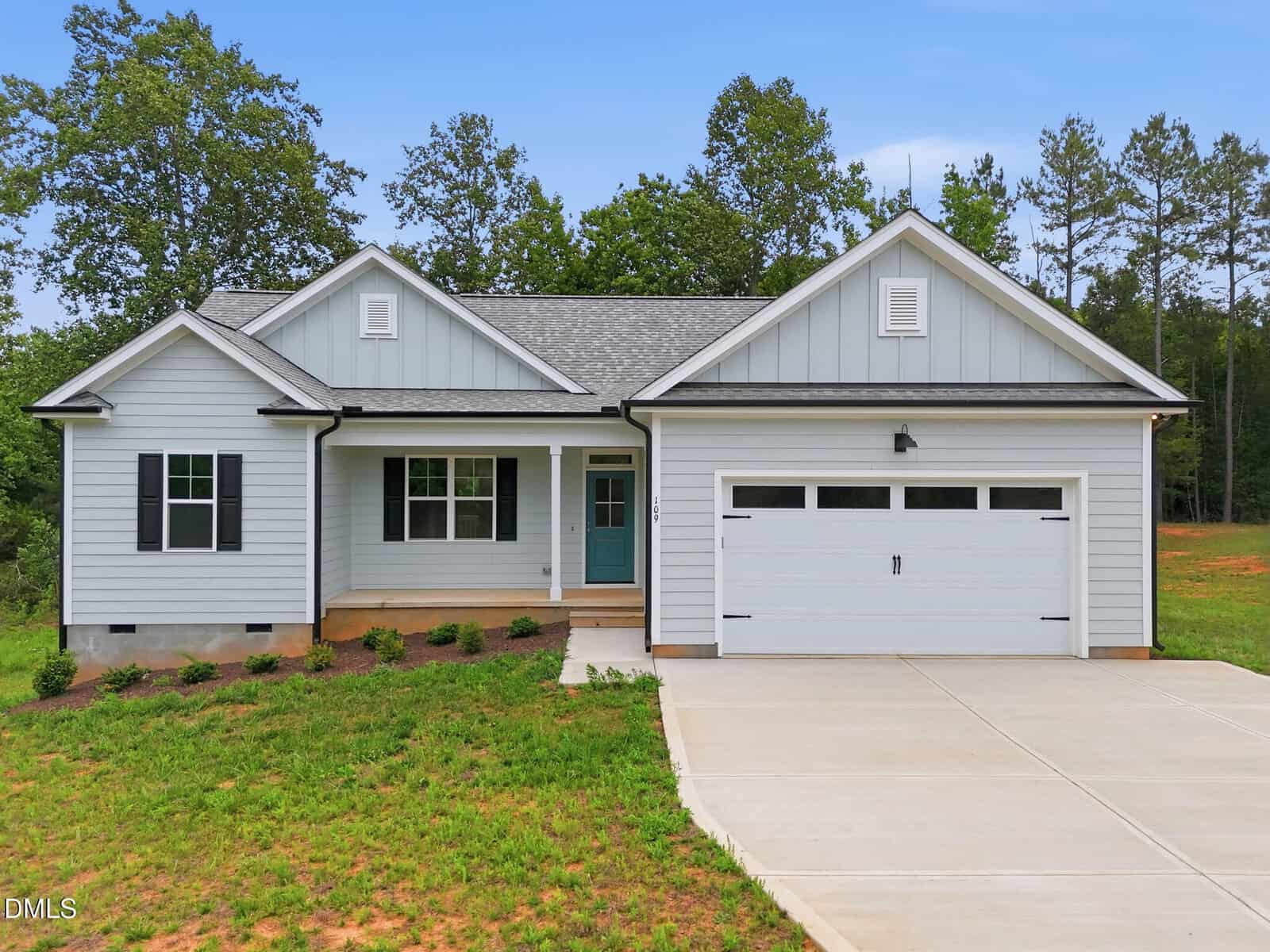 A modern single-story house at 109 Nutbush Creek Lane, Norlina, featuring light gray siding, black shutters, a teal front door, and a two-car garage, set on a green lawn with a concrete driveway and trees in the background.