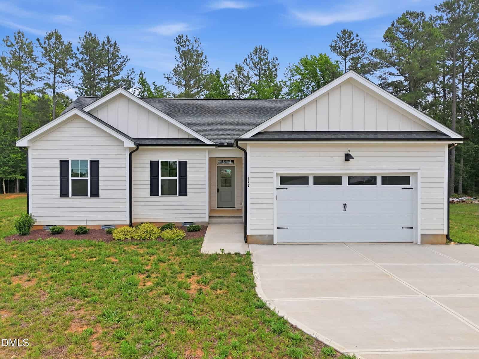 Single-story white house with black shutters and a double garage, located at 117 Nutbush Creek Lane in Norlina, surrounded by a grassy yard and trees in the background under a blue sky.