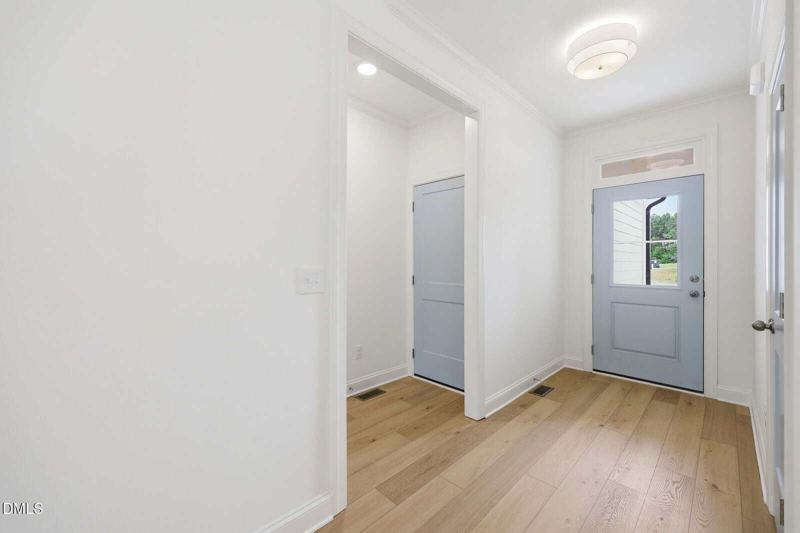 A bright hallway with light wood floors, white walls, two closed light blue doors on the left, and a matching blue front door with a window and transom, letting in natural light.