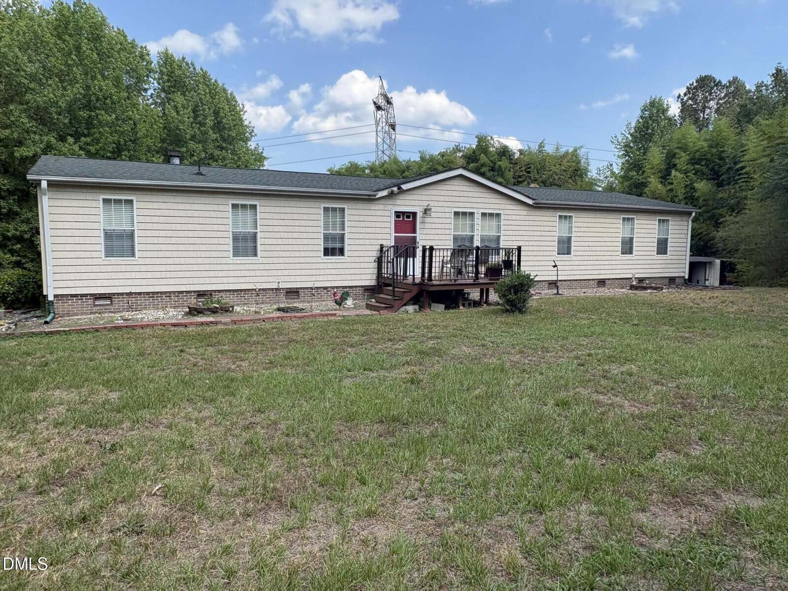 Charming single-story beige house with green roof at 1420 Ferrells Bridge Road, Louisburg, featuring a red front door and small raised deck with steps, set in a grassy yard surrounded by trees and a blue sky background.