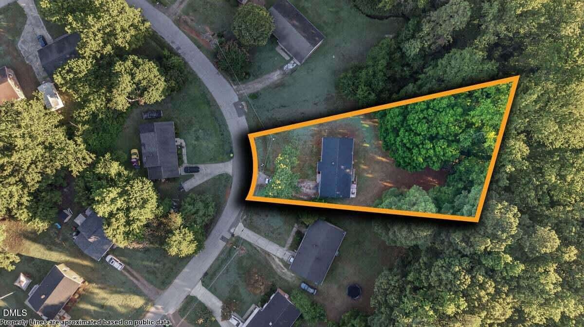 Aerial view of a residential neighborhood with a single house highlighted in an orange outline, surrounded by trees and neighboring homes. The highlighted property forms a wedge shape.