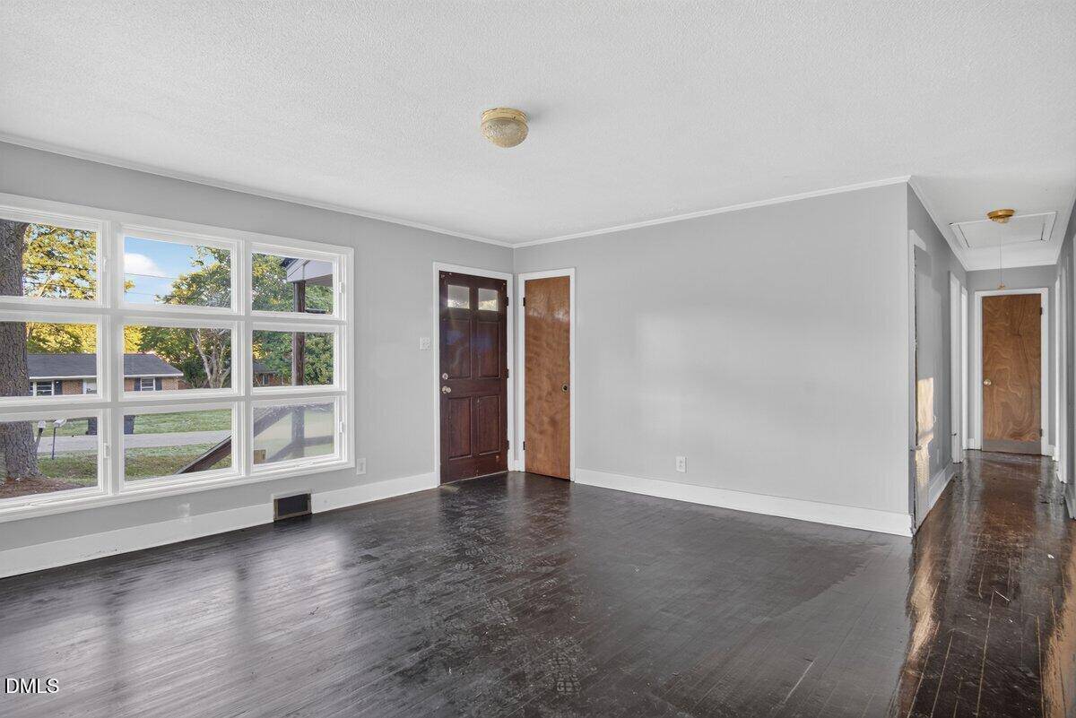 Bright living room with large windows, dark wood floors, neutral walls, wooden doors, and a ceiling light; sunlight streams in from outside, illuminating the space.