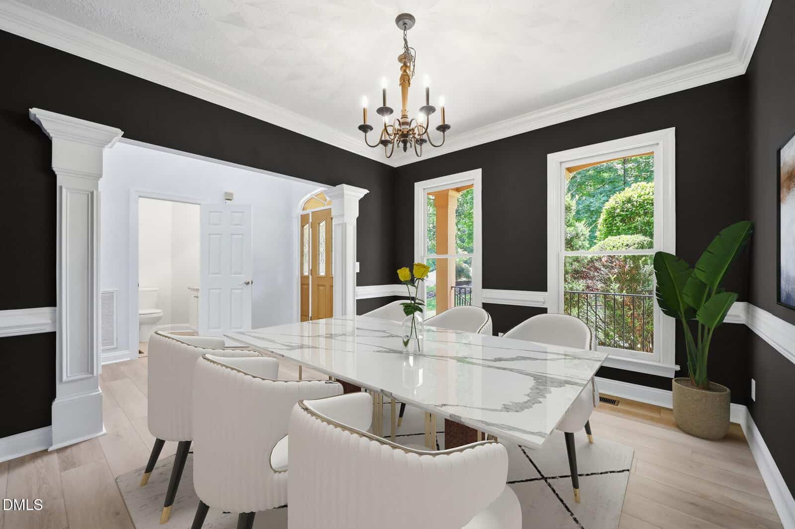 Elegant dining room with black and white walls, a marble table, six white chairs, a gold chandelier, large windows, a potted plant, and light wood floors. Natural light brightens the space.