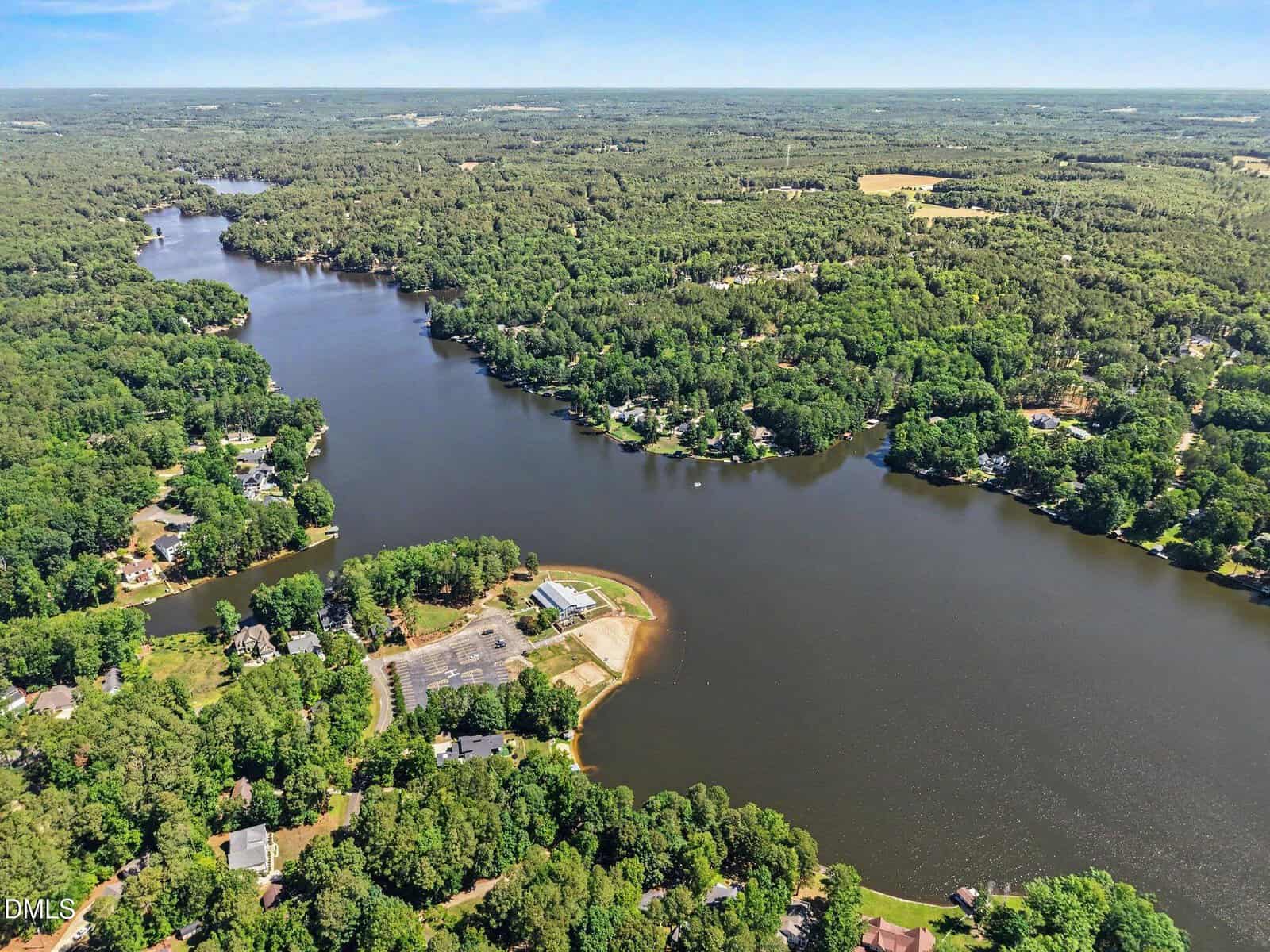 Aerial view of a winding river surrounded by dense forests and scattered houses, including those near 169 Black Cloud Drive, Louisburg, with a small peninsula extending into the water and a parking lot visible near the shoreline.