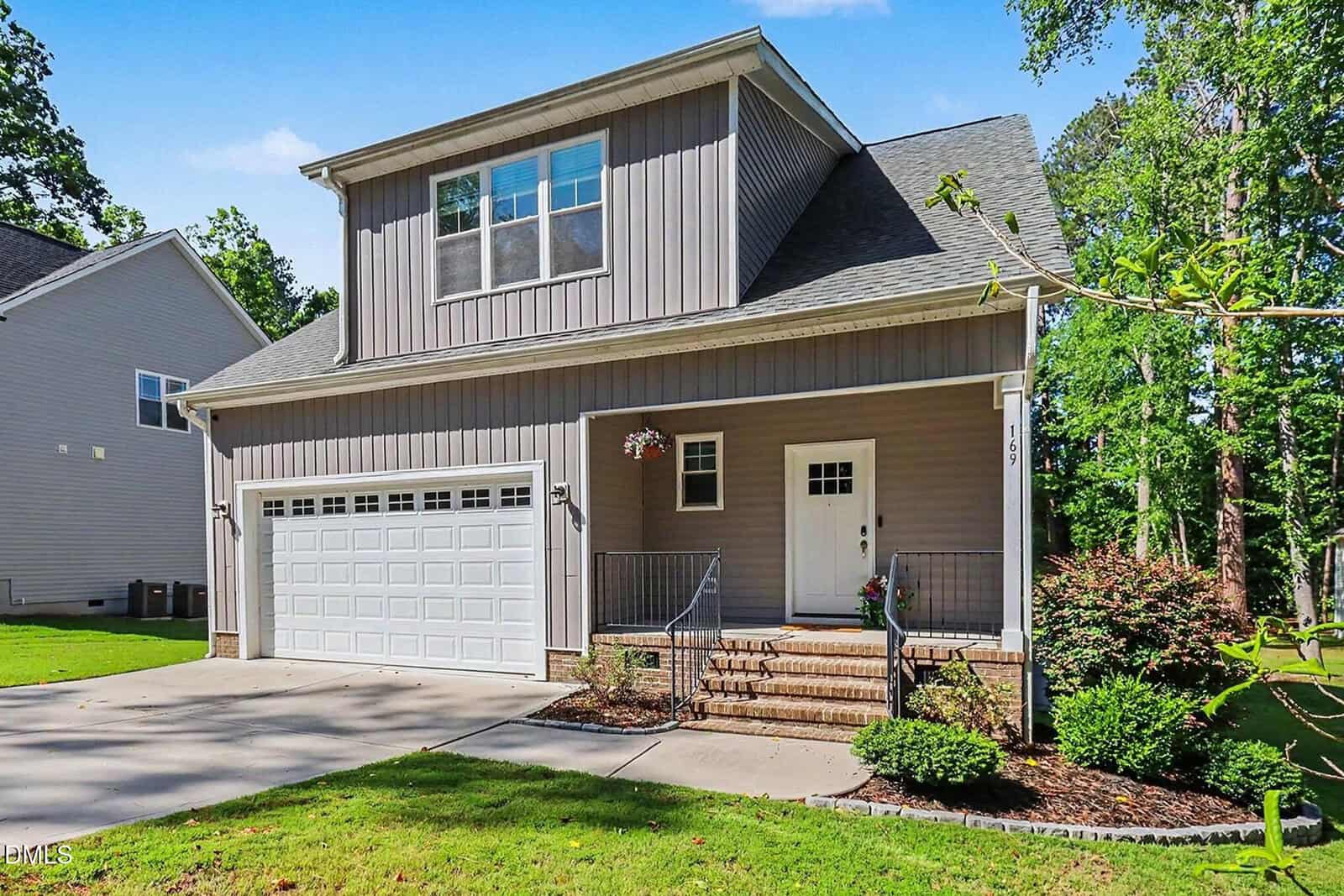 A modern, two-story gray house at 169 Black Cloud Drive, Louisburg, features a two-car garage, small front porch, and neatly landscaped yard in a charming suburban neighborhood with lush grass and trees in the background.