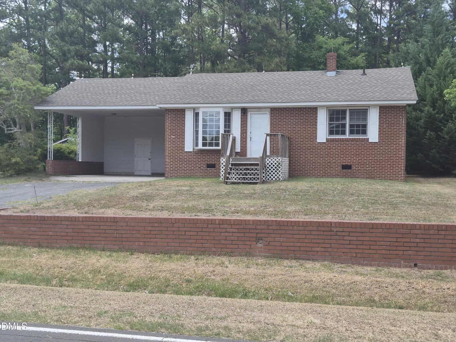 A single-story brick house with white trim at 109 Moss Road in Creedmoor, featuring a small front porch and attached carport, set on a grassy lawn with a low brick wall by the roadside. Pine trees line the background.