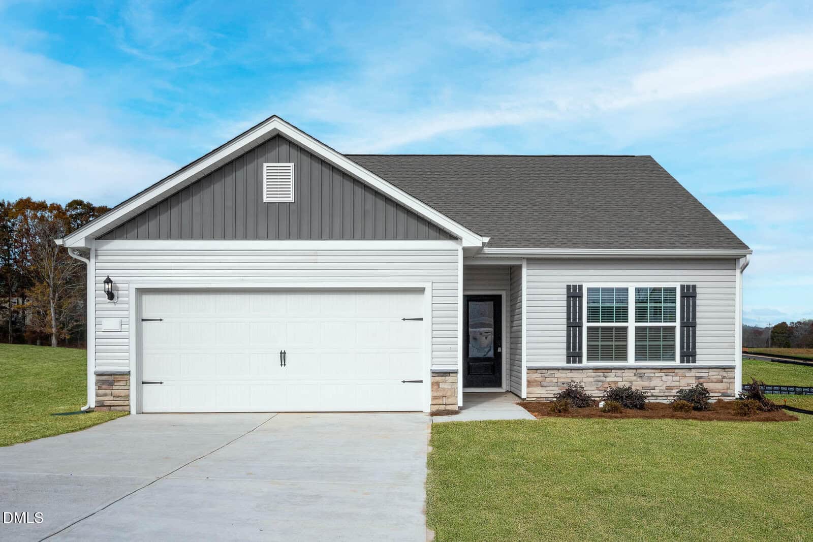 A modern, single-story house at 112 Independence Lane, Oxford, with gray siding, a dark shingled roof, and a double garage. Enjoy a driveway, small front porch, and newly landscaped yard with grass and shrubs under a blue sky.