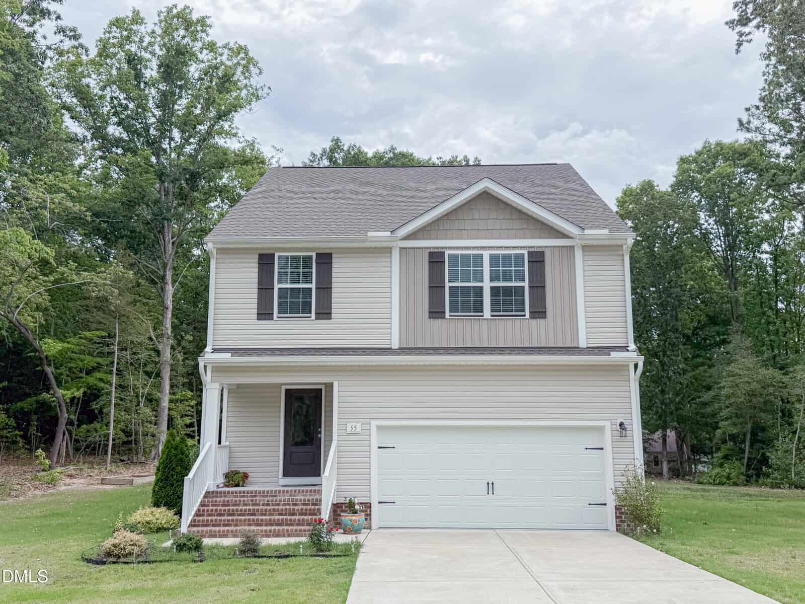 Charming two-story suburban house at 55 Shearin Lane, Youngsville, with beige siding, brown shutters, and a white double garage door. A small porch welcomes you, surrounded by a green lawn and trees.