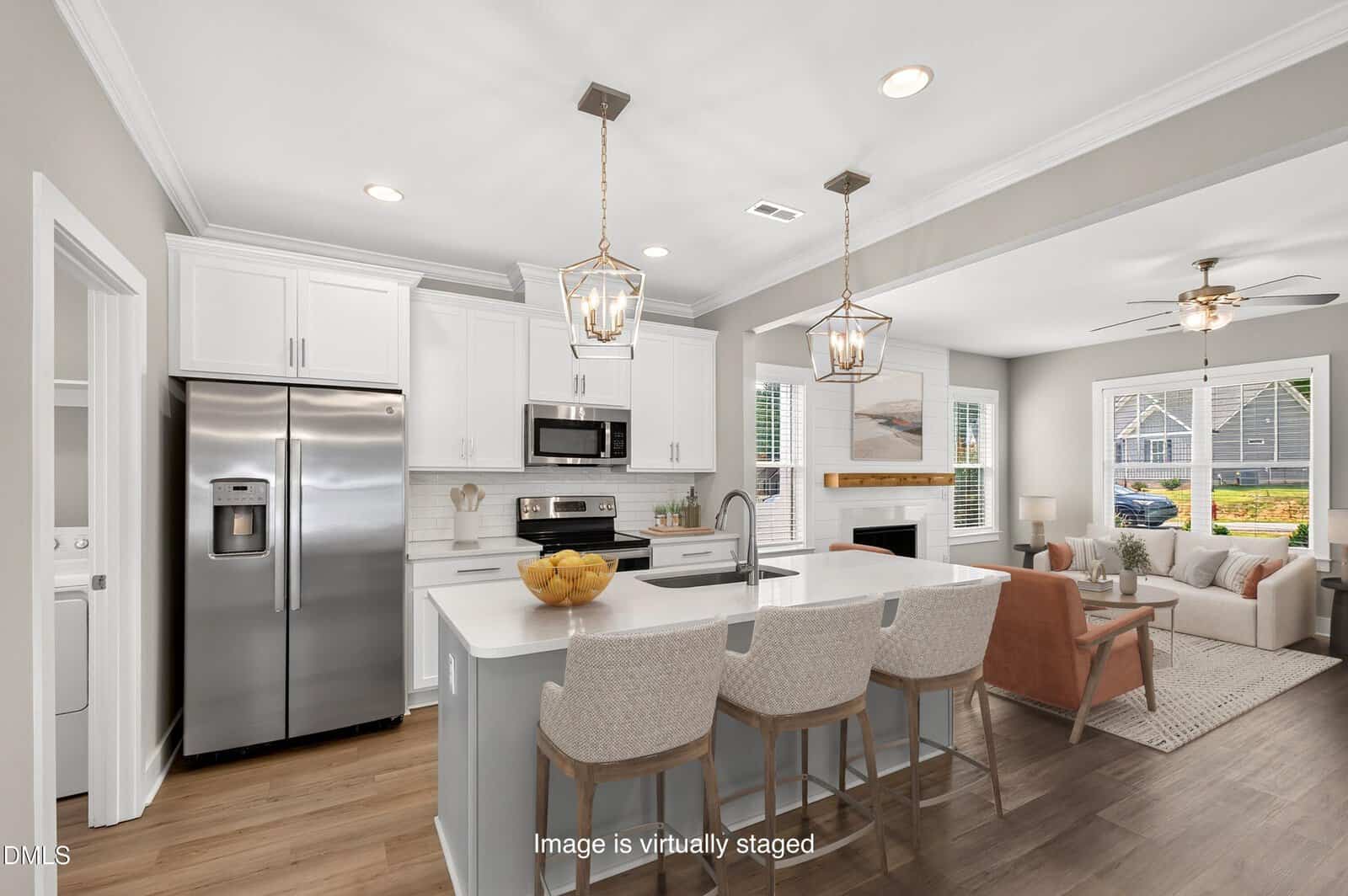 Modern kitchen with white cabinets, stainless steel appliances, an island with barstools, and a cozy living area with a sofa, chairs, and large windows. This bright and stylish space is located at 101 Averly Court in charming Stem.