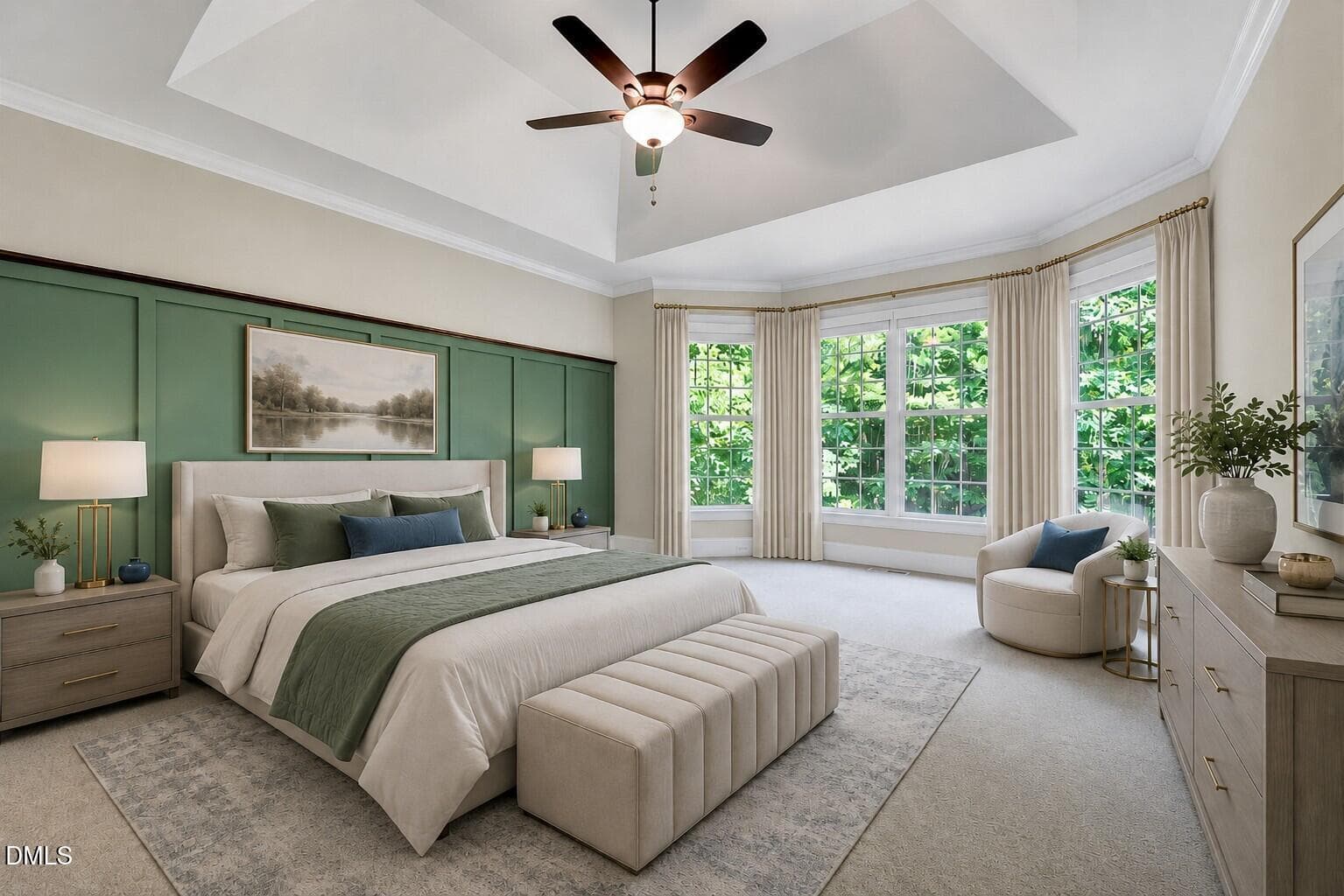 A spacious, modern bedroom with a large bed, green accent wall, artwork, two nightstands with lamps, a bench at the foot of the bed, a dresser, cozy chair by bay windows, and greenery visible outside.