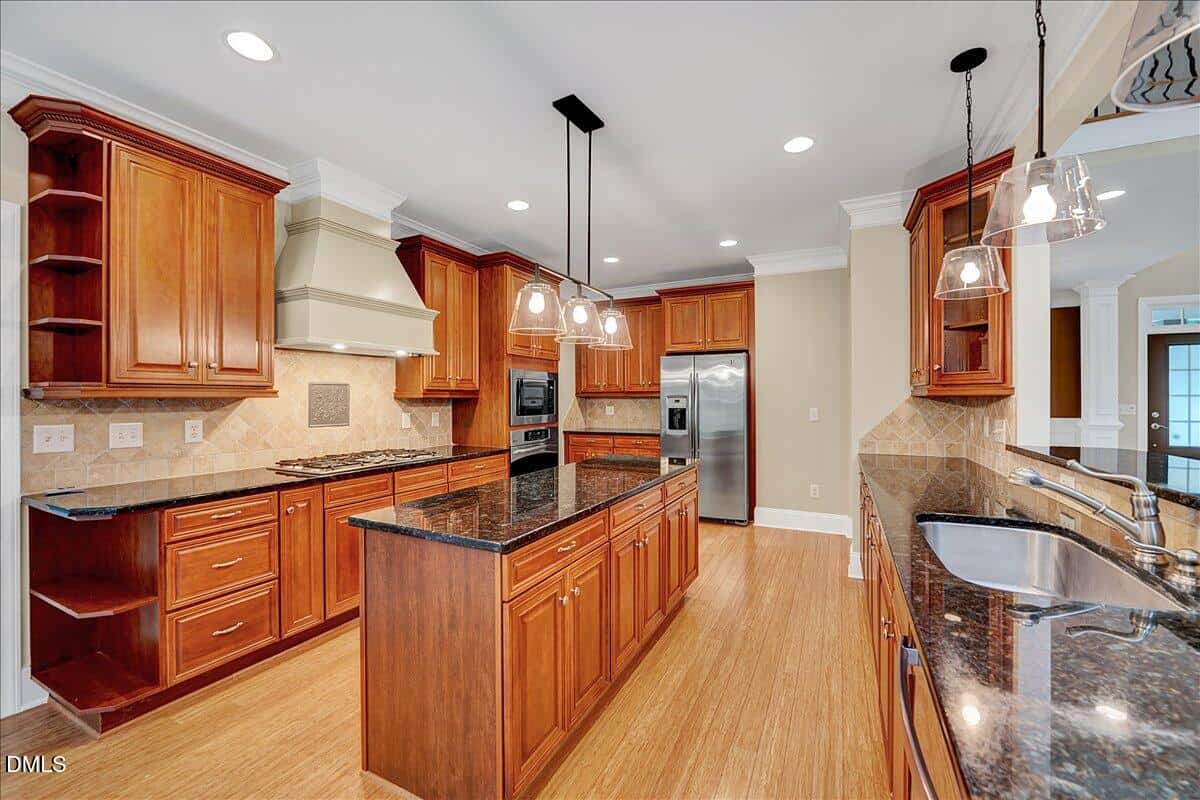 Spacious kitchen with wood cabinets, granite countertops, a central island, stainless steel appliances, built-in oven, tiled backsplash, pendant lights, and hardwood floors.