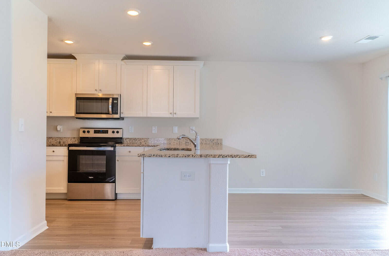 Modern kitchen with white cabinets, stainless steel appliances, granite countertops, and a large island; light wood flooring and neutral walls create a bright, open space.