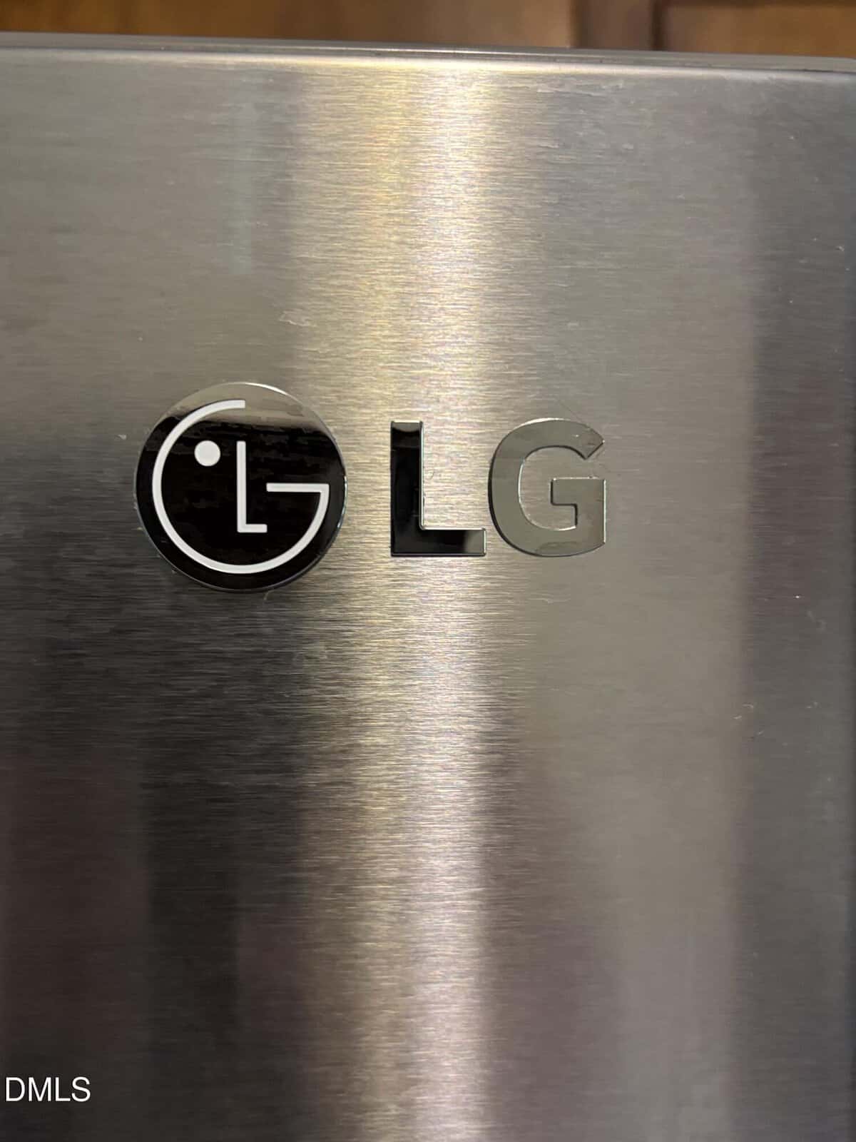 Close-up of an LG logo on a stainless steel surface, likely part of a household appliance, with a brushed metal texture and some light reflections.