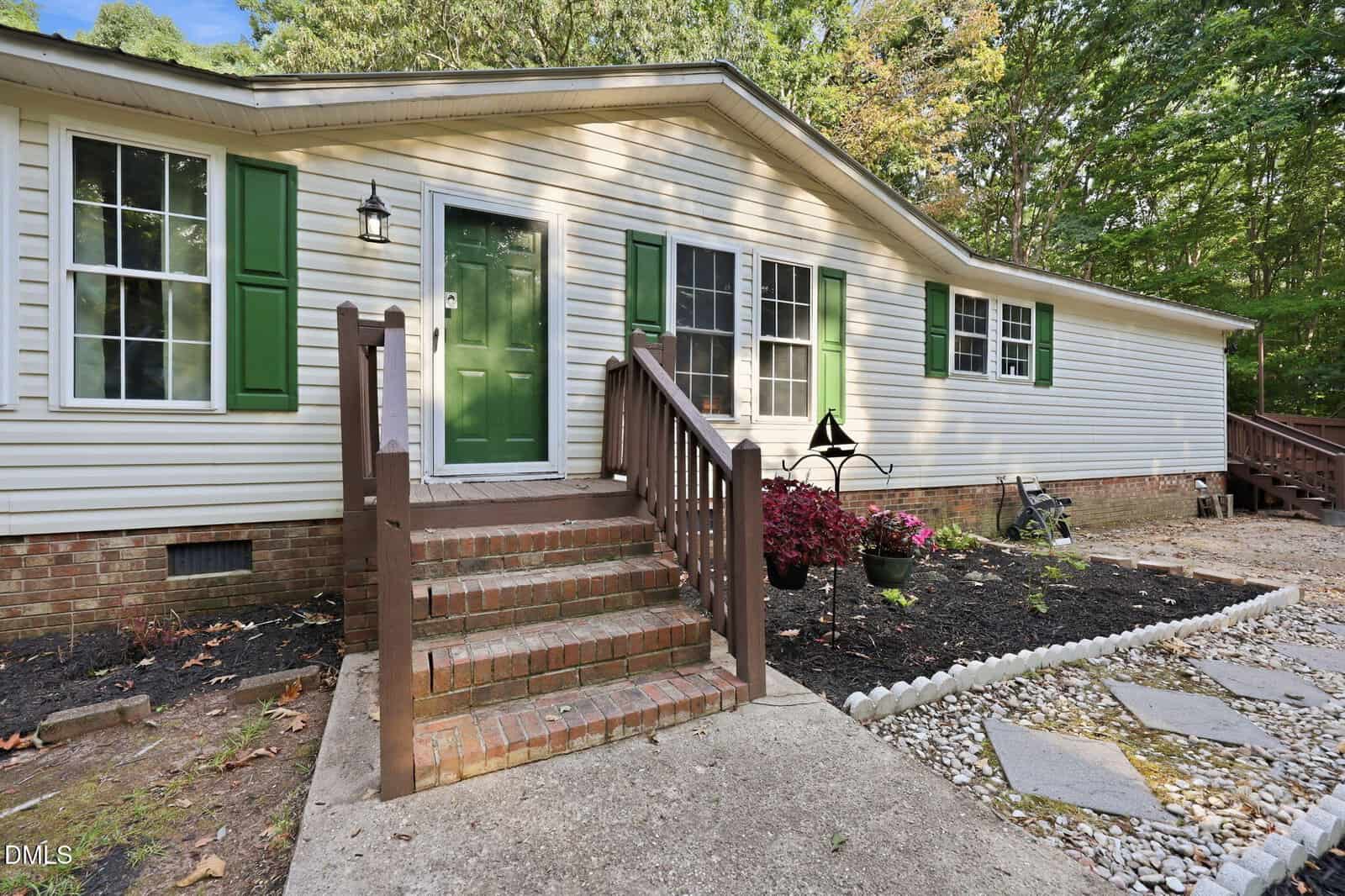 Front view of a single-story house at 109 Nature Trail, Louisburg, with beige siding, green shutters, and a green door. A brick staircase with wooden railings leads to the entrance, complemented by potted plants and landscaped rocks.