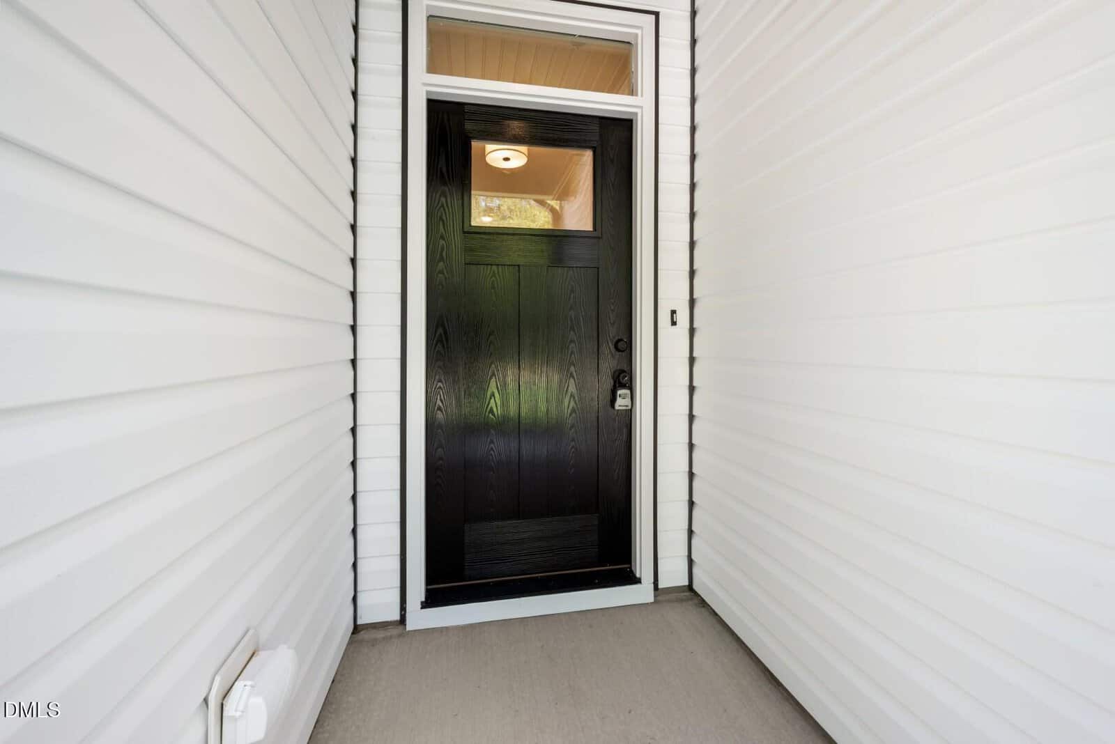 A modern black front door with a silver handle and a small window at the top, surrounded by white siding, seen from a covered porch area.