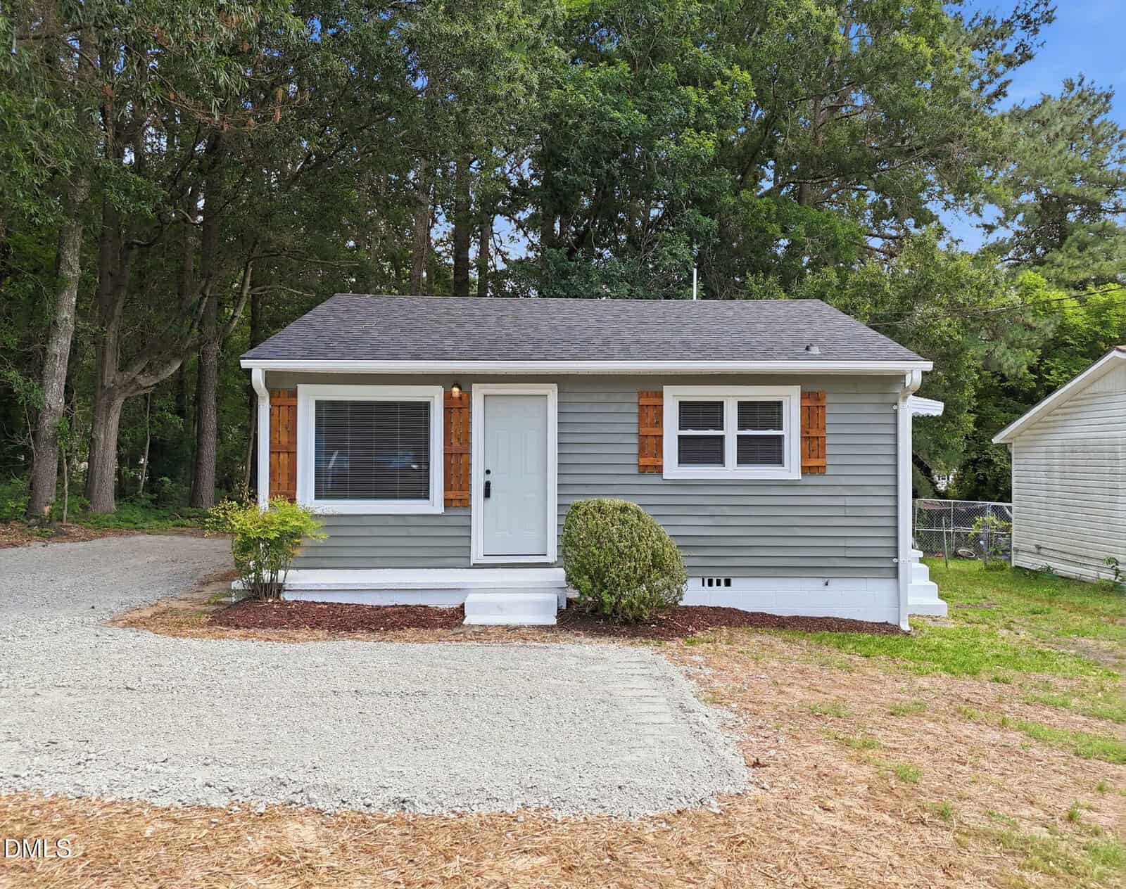 Charming small gray house with white trim and wooden shutters at 149 S Elizabeth Street, Henderson. Features a white front door, gravel driveway, and a few shrubs in front, all surrounded by trees and greenery.