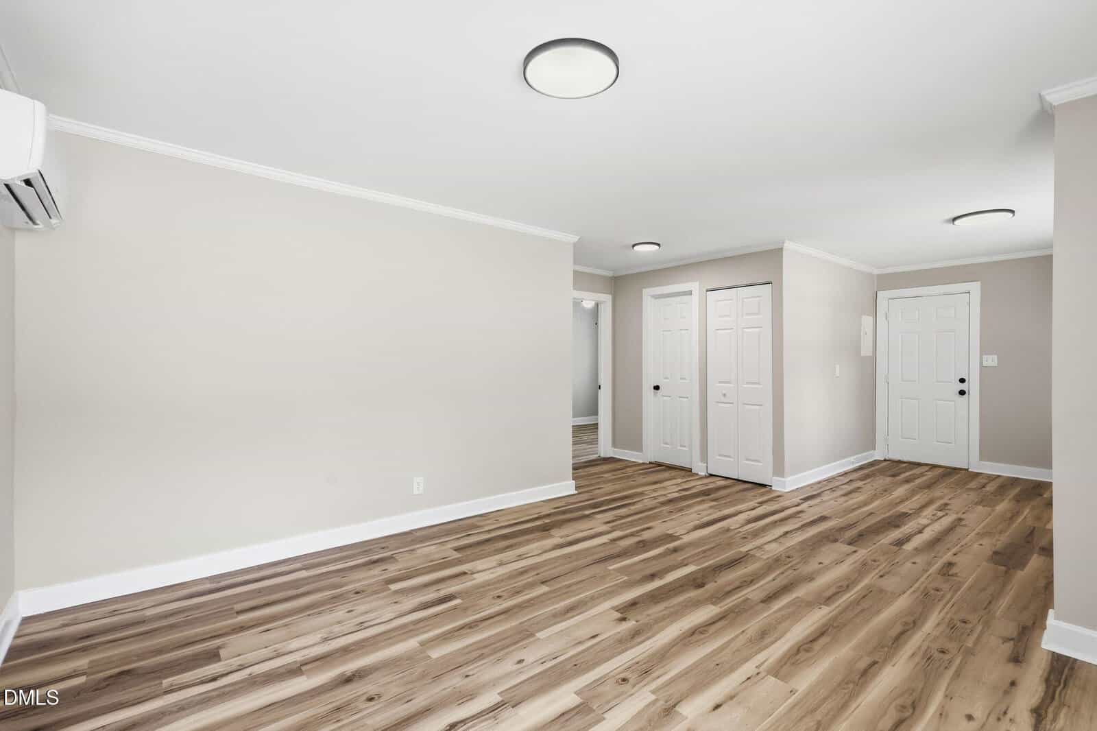Unfurnished room with light beige walls, wood-style flooring, two ceiling lights, a white door, two white double closets, and a wall-mounted air conditioning unit.