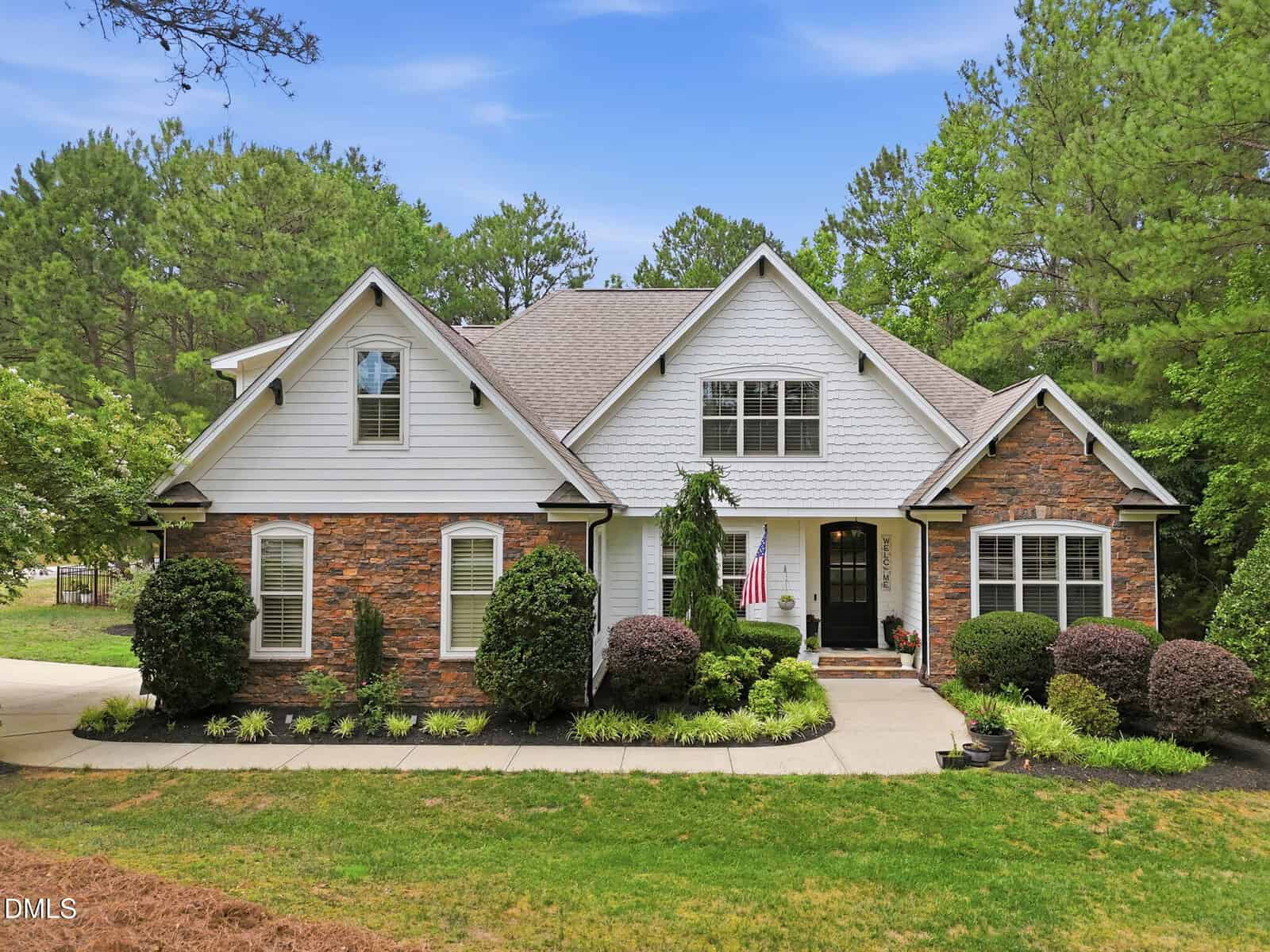 A two-story suburban house with white siding and brick accents at 60 Granite Drive in Franklinton, surrounded by neatly trimmed bushes and trees. An American flag hangs near the front door, and a curved driveway leads to the entrance.