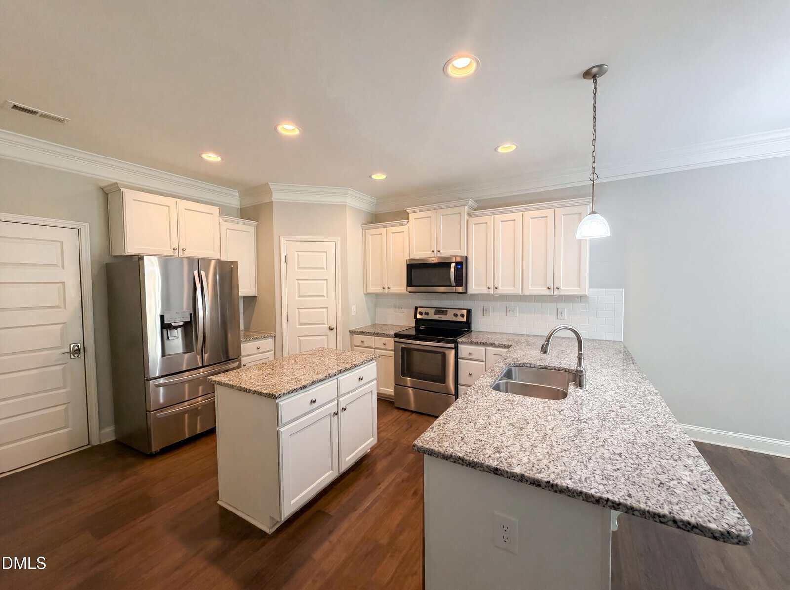 Modern kitchen with white cabinets, stainless steel appliances, a central island, granite countertops, and recessed lighting. The floor is wood, and the room is bright with ample natural and artificial light.