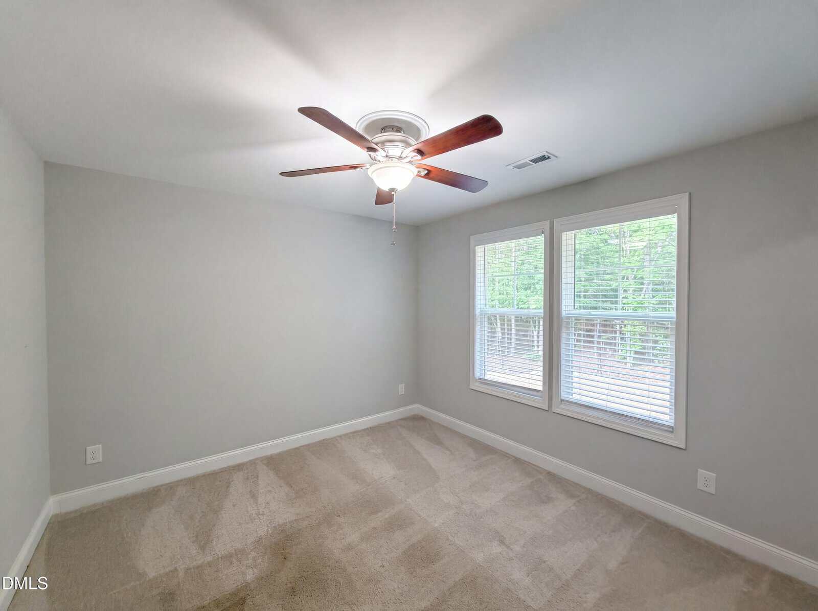 Empty room with beige carpet, light gray walls, a ceiling fan with lights, and two large windows with blinds letting in natural light.