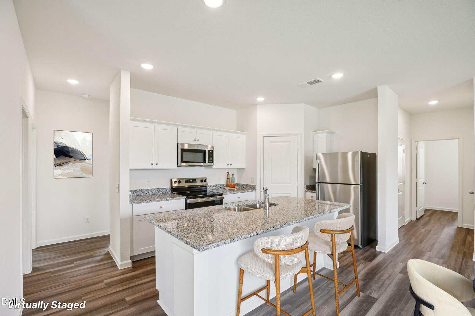 A modern kitchen with white cabinets, stainless steel appliances, granite countertops, and an island with two cushioned bar stools. The flooring is wood and the space is bright with recessed lighting.
