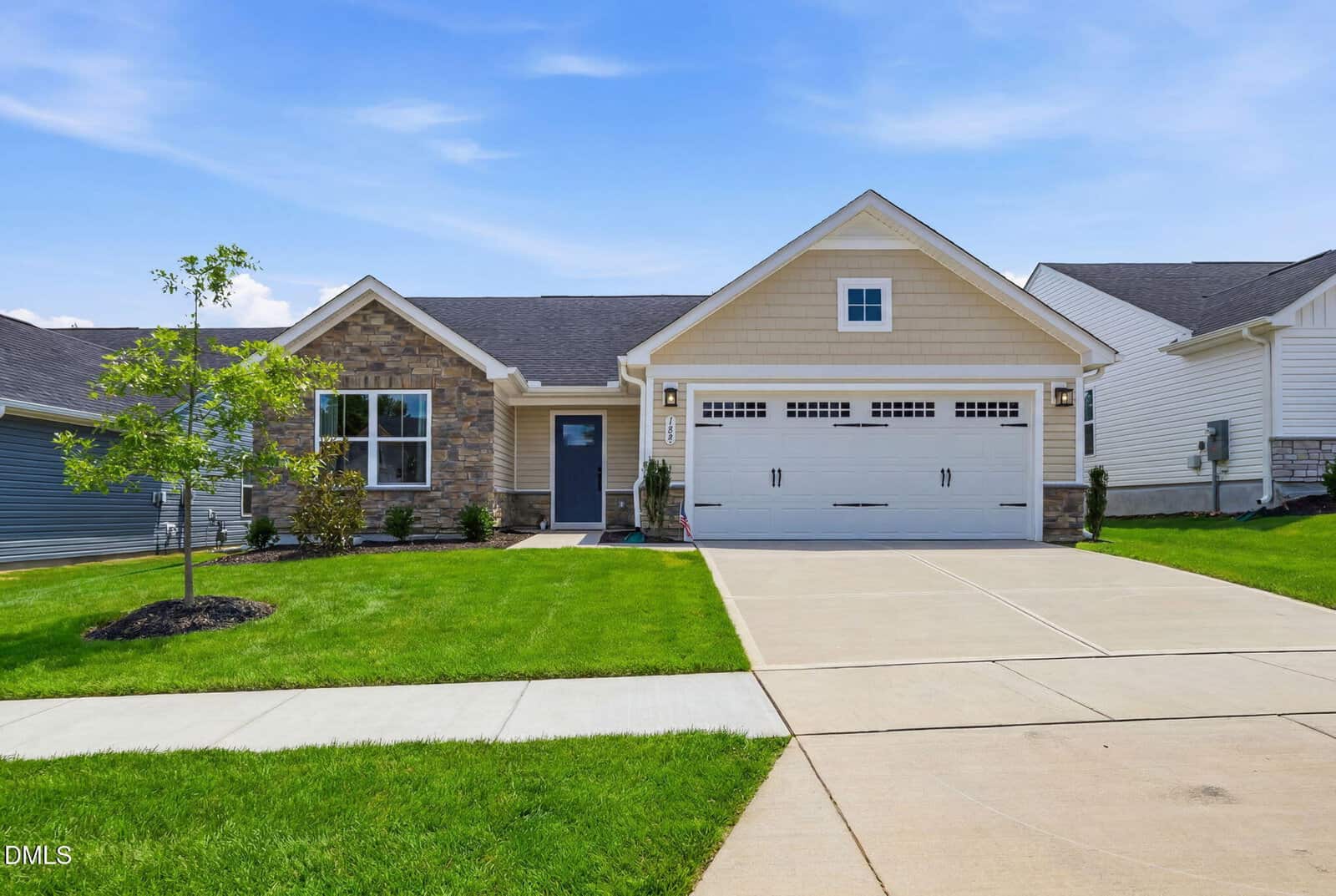Single-story suburban house with stone and tan siding, a double garage, and a manicured green lawn, on a sunny day with a blue sky.