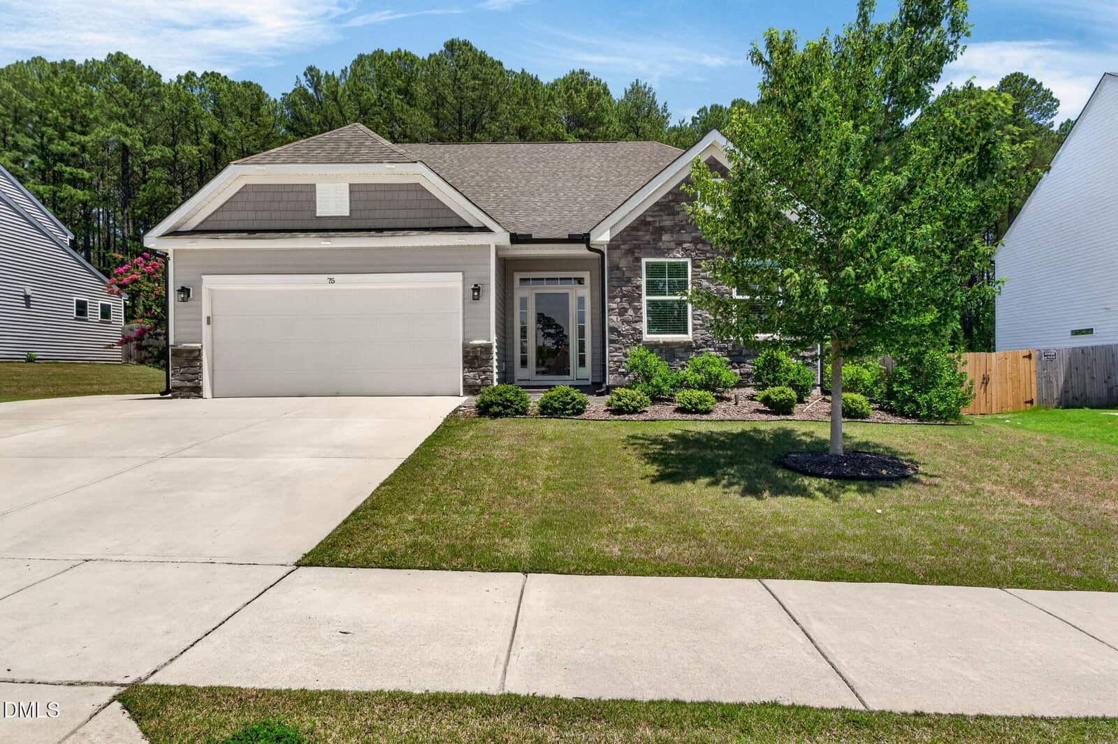 Charming single-story home at 75 Mallory Oak Drive, Franklinton, featuring a two-car garage, stone and siding exterior, small front porch, neatly trimmed shrubs, young tree, plus a concrete driveway and sidewalk leading to the entrance.