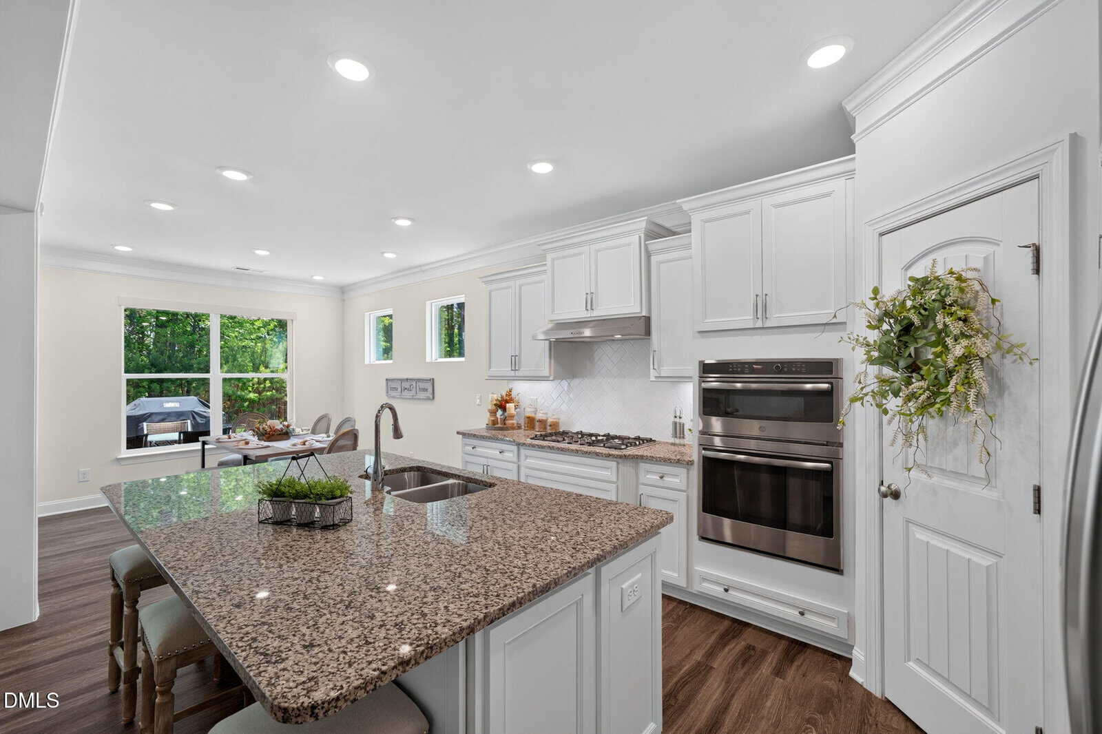 Modern kitchen with white cabinets, granite countertops, a large center island with barstools, built-in double ovens, a gas cooktop, stainless appliances, wood floors, and large windows letting in natural light.
