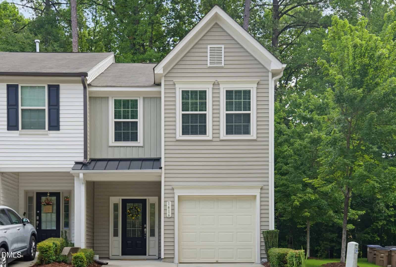 A two-story beige townhouse at 1416 Chatuga Way, Wake Forest, with white trim, black roof accents, and a one-car garage. Two upstairs windows and a black front door with side windows overlook green trees and a well-kept lawn.