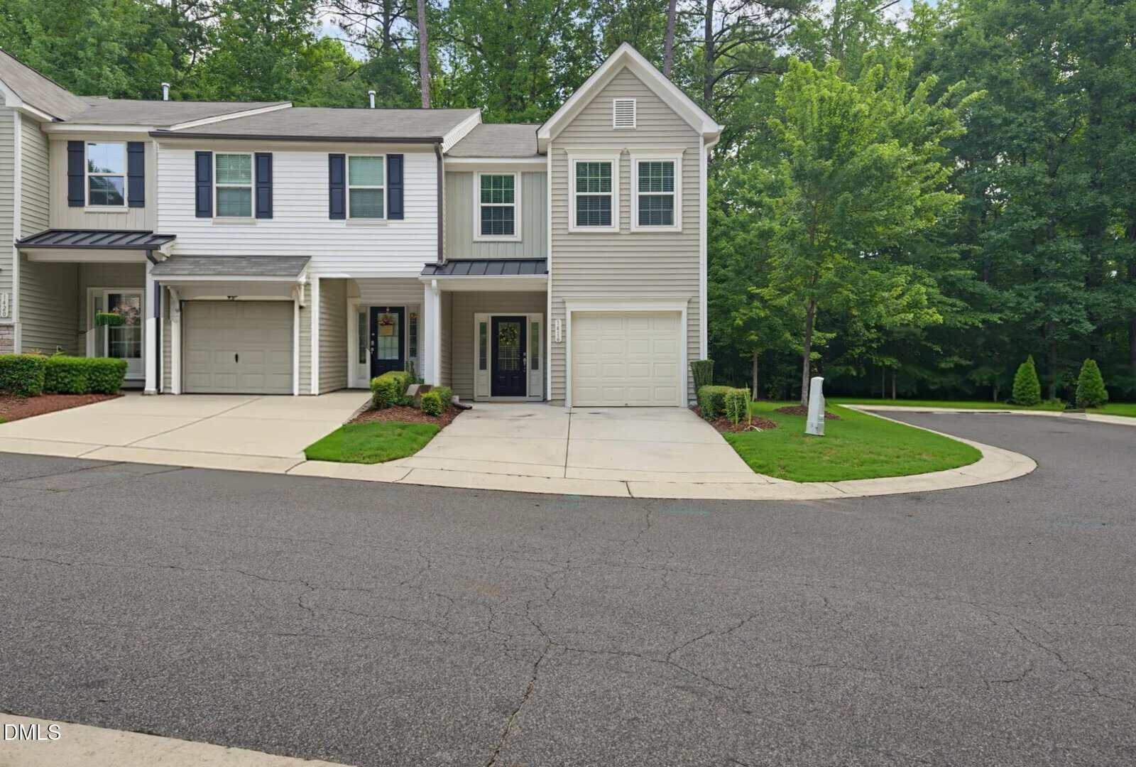 A two-story townhouse with gray siding, a single-car garage, and a small front yard, located at the corner of a quiet, tree-lined street.
