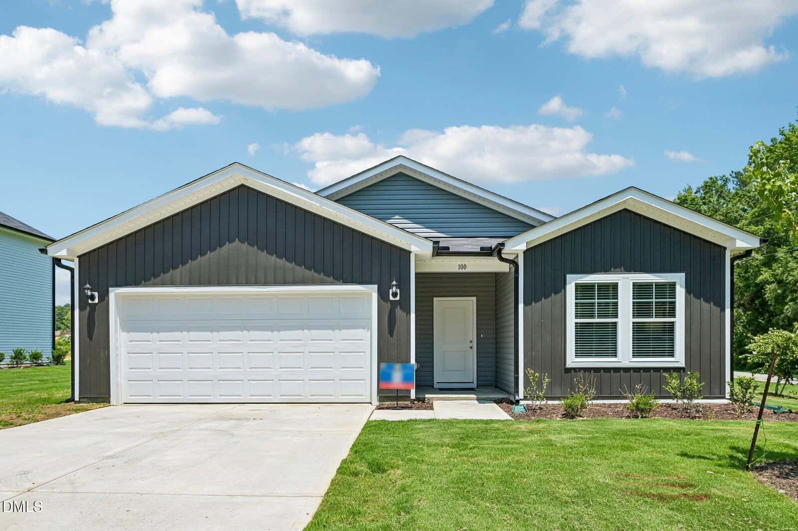 Located at 106 Airdale Drive in Oxford, this single-story house features dark gray siding with crisp white trim and a spacious double garage. Two front windows and a charming small porch add to its curb appeal, while the well-maintained driveway and lush lawn create an inviting entrance. Mature trees frame the property, set against a backdrop of blue sky with scattered clouds.
