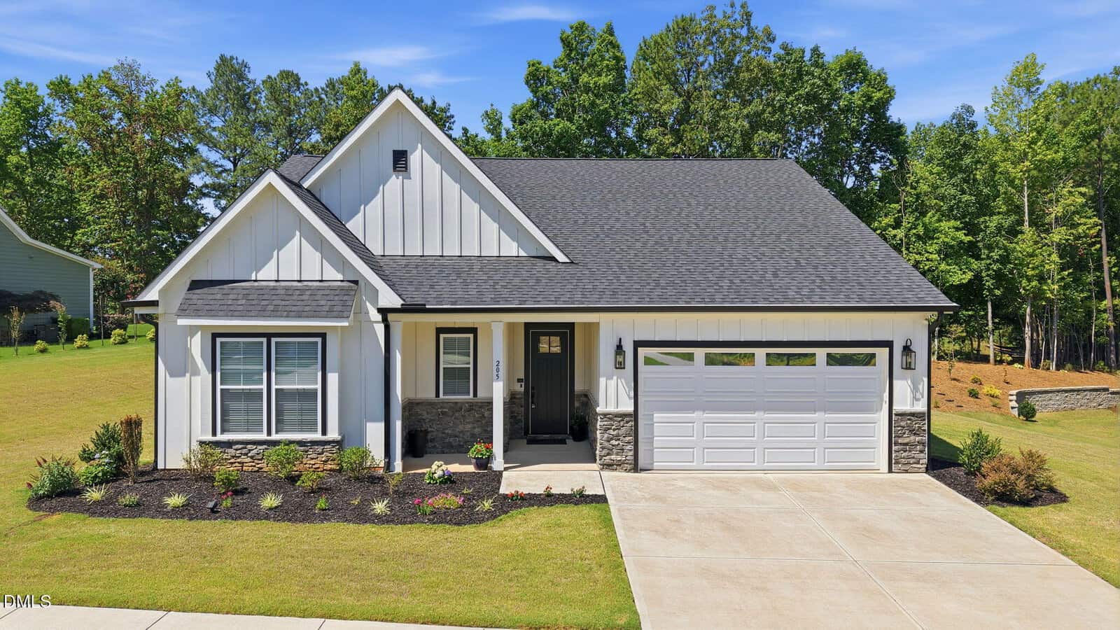A modern single-story house at 205 Sutherland Drive, Franklinton, with white siding, black trim, stone accents, and a double garage. The home features a manicured lawn, concrete driveway, and is surrounded by trees under a clear blue sky.
