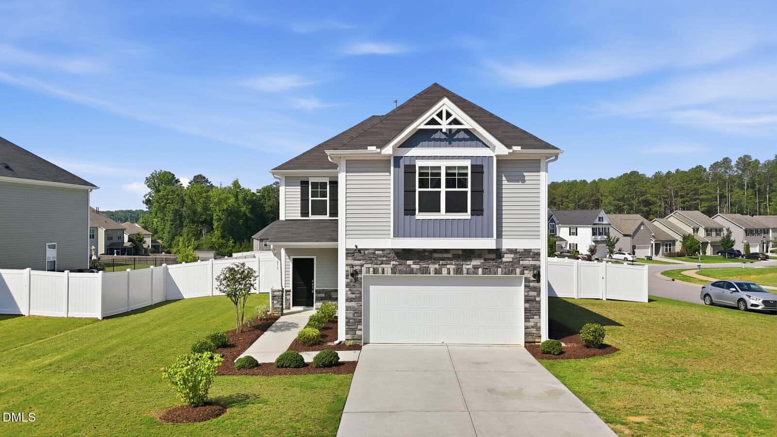 A two-story suburban house with gray siding, stone accents, and a double garage at 675 Hawksbill Drive in Franklinton. It features a well-maintained lawn, white fenced backyard, and sits in a residential neighborhood under a blue sky.