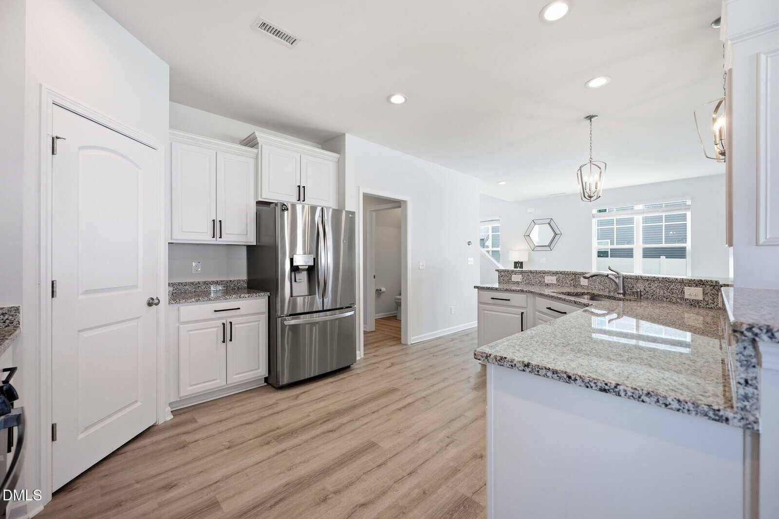 Modern kitchen with white cabinets, stainless steel appliances, granite countertops, and light wood flooring. Large windows and pendant lights provide ample natural and artificial light.