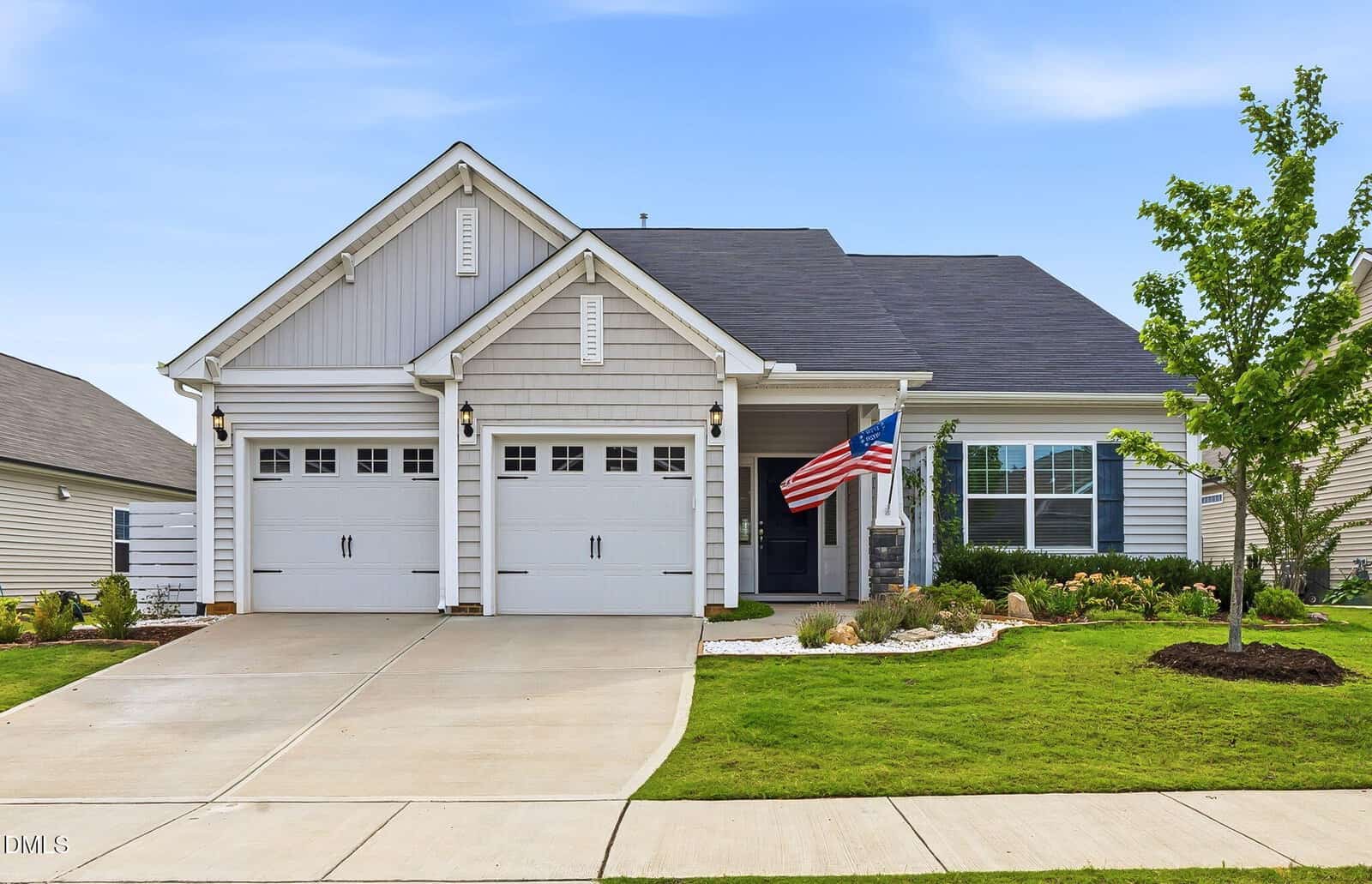 A modern, single-story house at 40 Waterclover Path in Youngsville features two garage doors, a well-kept lawn, a small tree, landscaped garden beds, and an American flag mounted near the front porch under a partly cloudy sky.