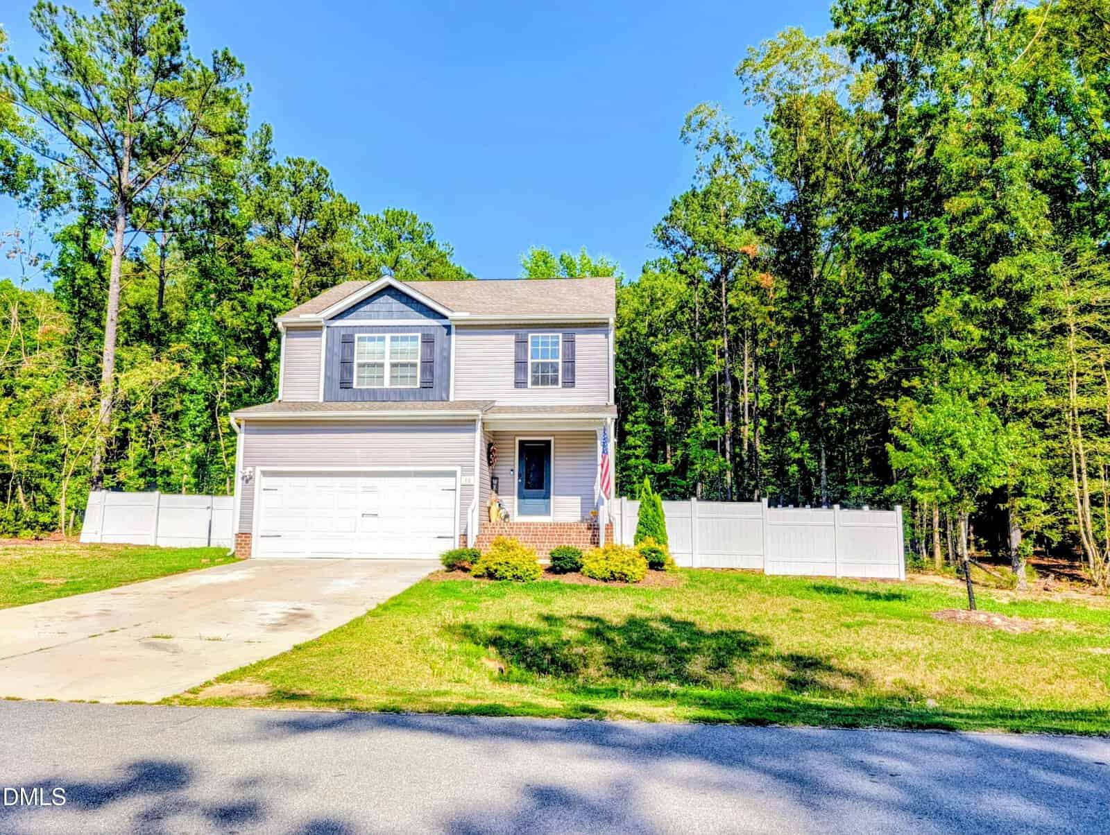 A two-story gray house at 30 Nandina Lane in Youngsville with a white garage and fenced yard, set on a sunny day with green trees behind and a well-kept lawn in front. An American flag hangs near the entrance.