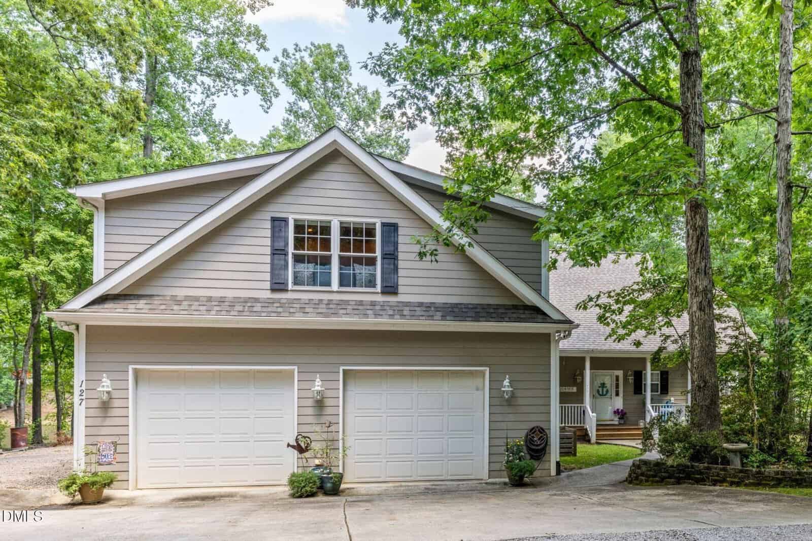 A two-story gray house with white trim and double garage sits among tall green trees at 127 S Daniel Court, Macon, with a driveway and steps leading to the front porch.
