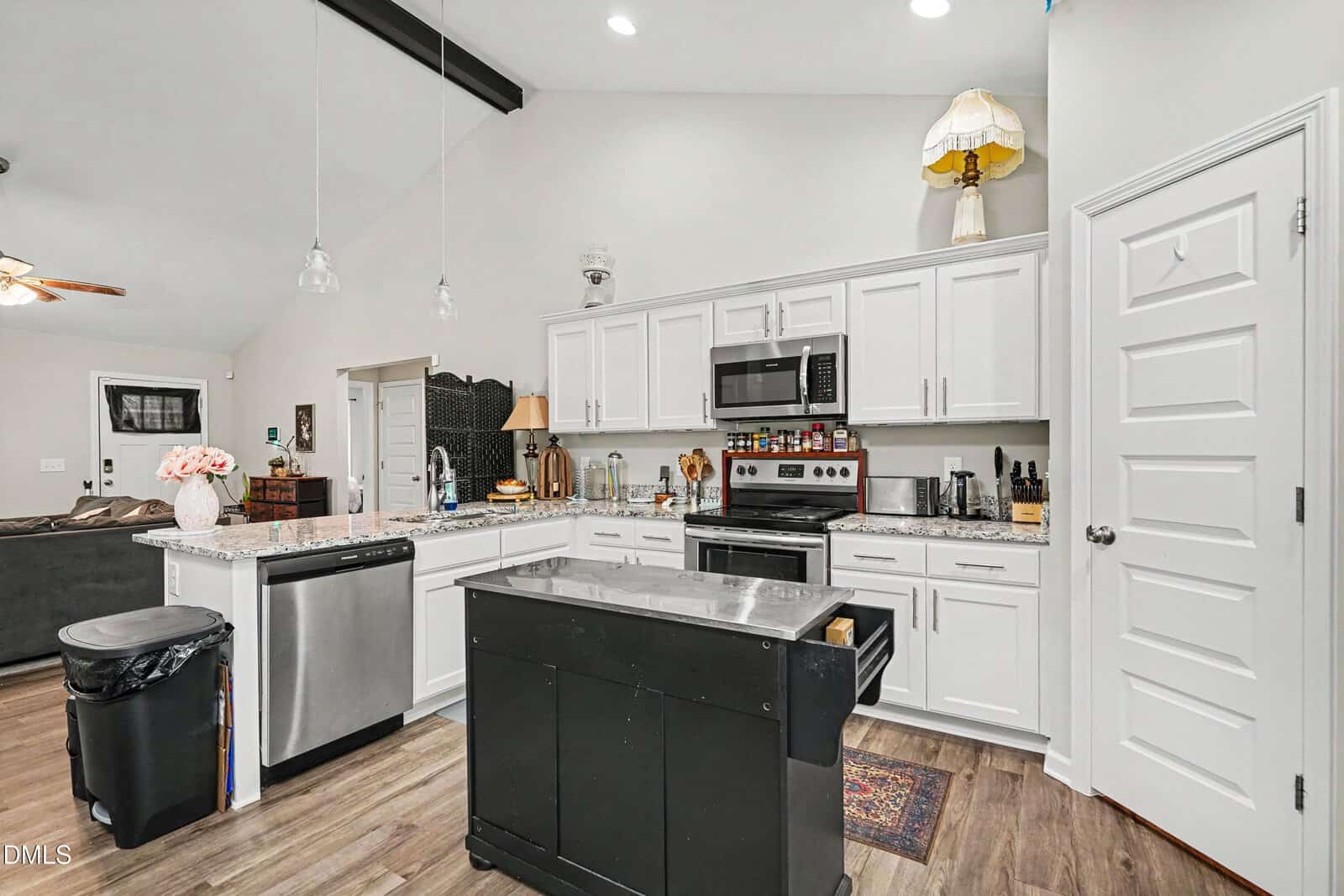 Modern kitchen with white cabinets, stainless steel appliances, a small black island, granite countertops, and a mix of classic and vintage decor items, including table lamps on the counters and a lamp above the cabinets.
